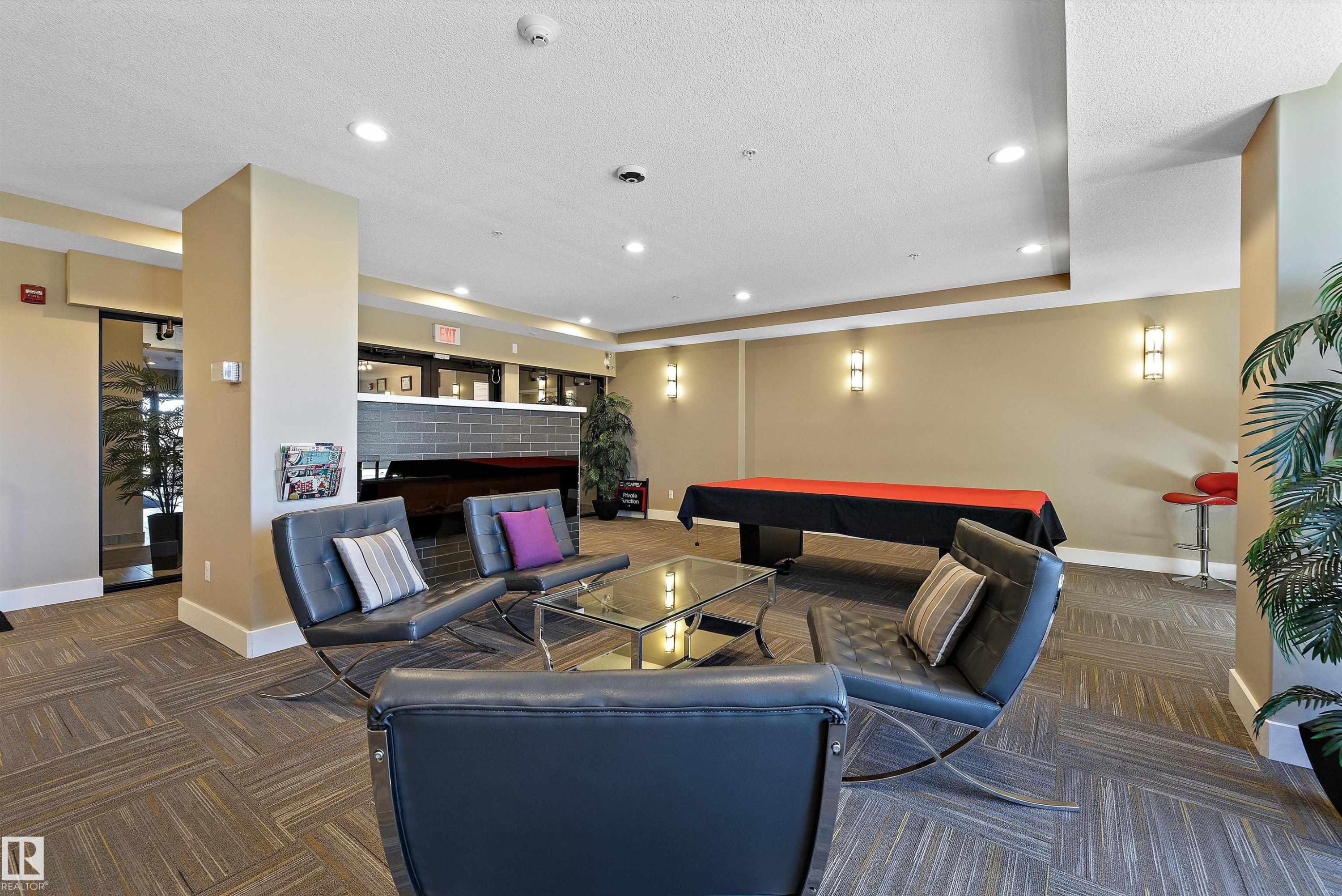 The Recreation Room has a modern kitchen featuring a striking red island countertop, stainless steel appliances, dark wood-finish cabinetry, and a dark subway tile backsplash, with a pool table and a lounge type seating to enjoy with your company. - 307 11080 Ellerslie Rd Sw, Edmonton, AB