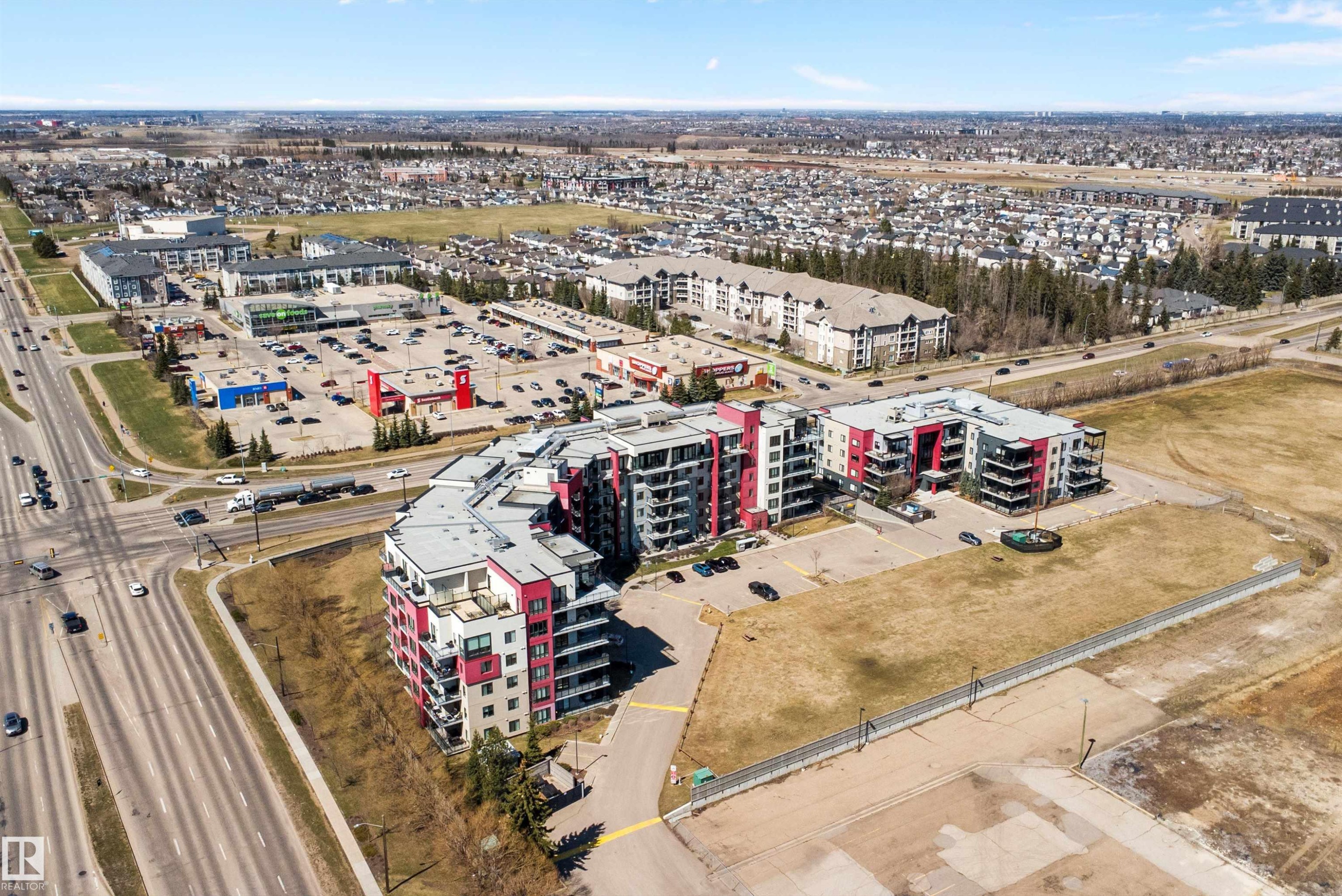 Modern multi-story residential buildings featuring contemporary architecture with vibrant red and gray facade panels. - 307 11080 Ellerslie Rd Sw, Edmonton, AB