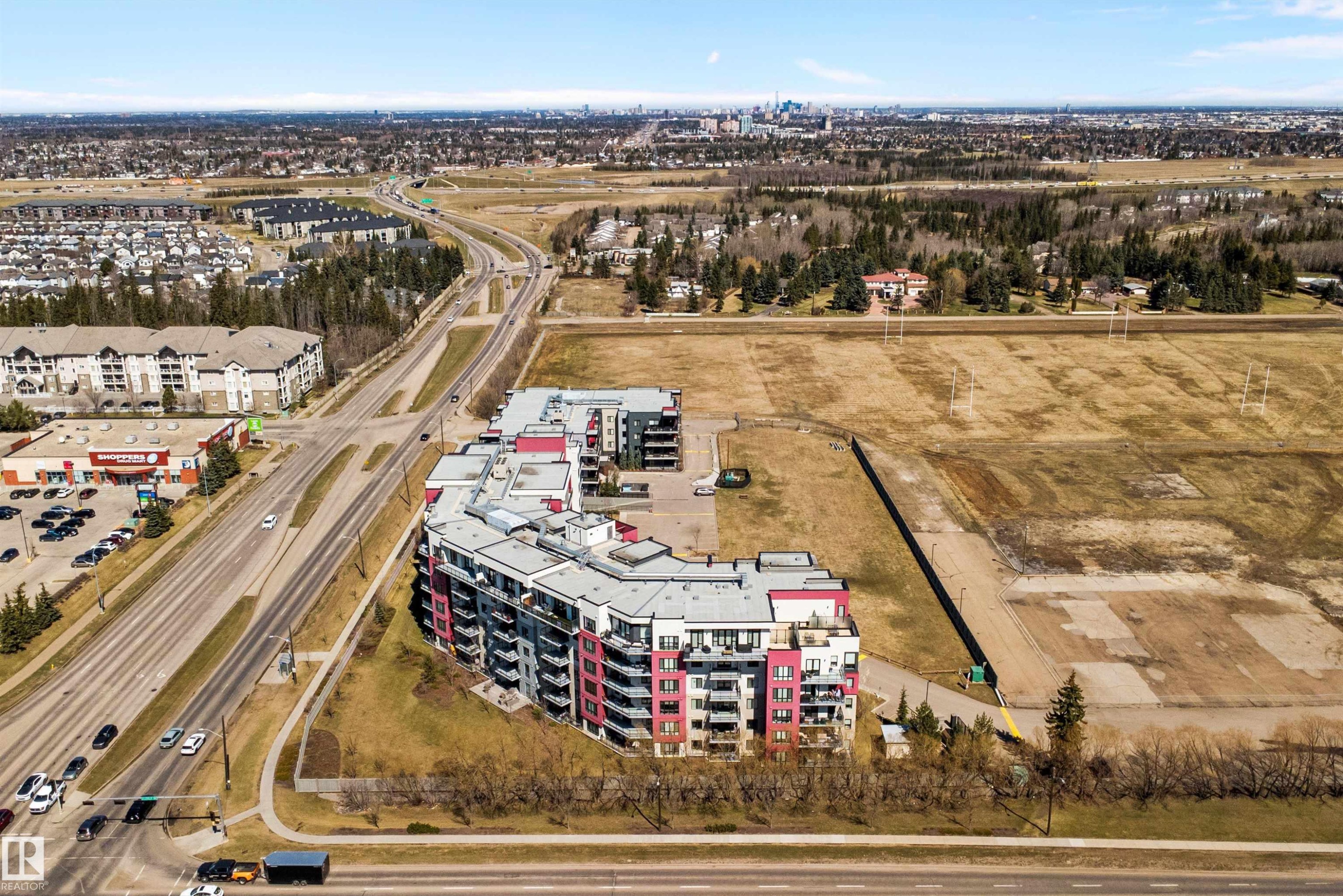 Curved residential building featuring a modern facade with red and white accents, multiple private balconies, and a flat roofline - 307 11080 Ellerslie Rd Sw, Edmonton, AB