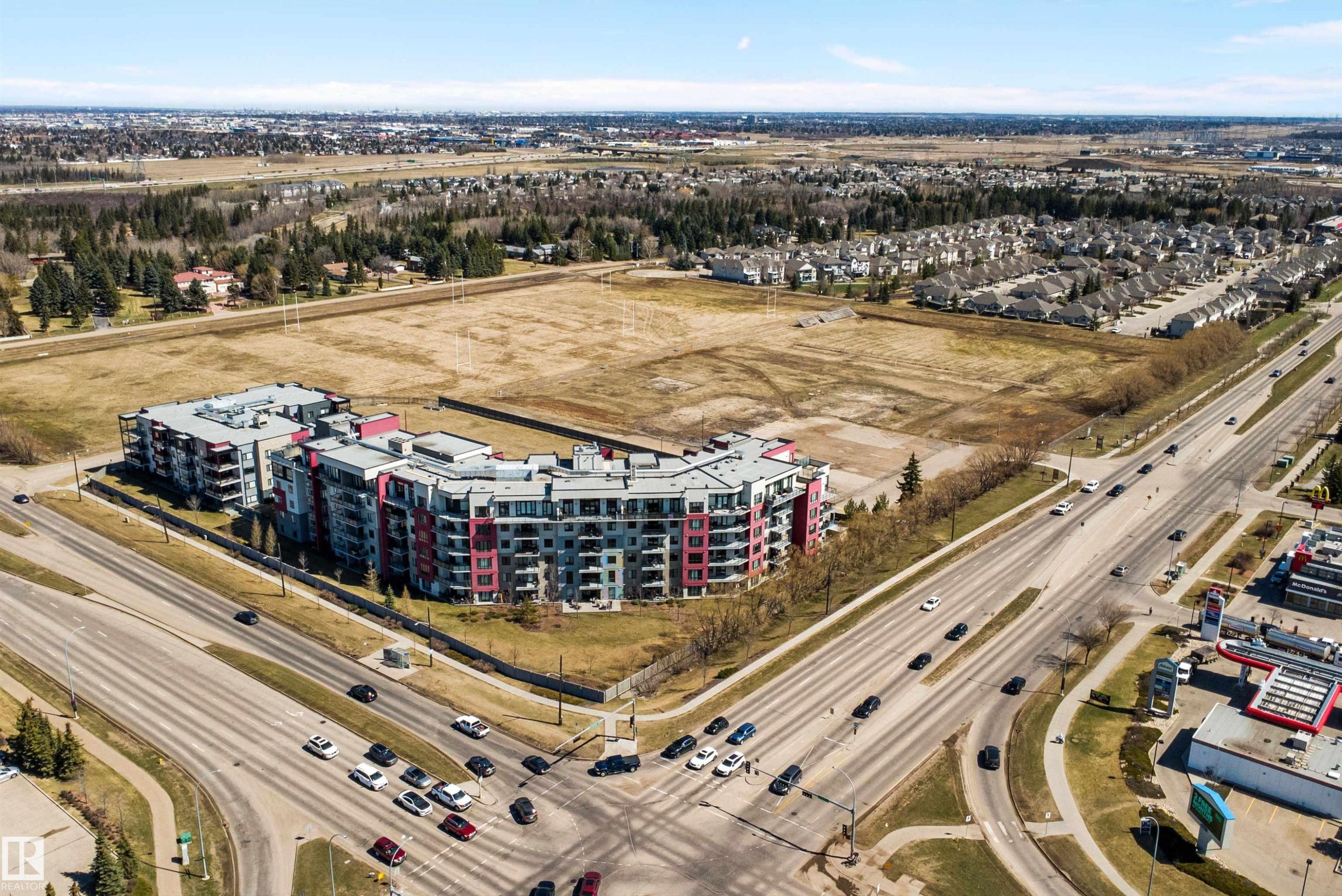 Modern multi-story residential buildings featuring contemporary architecture with vibrant red and gray facade panels. - 307 11080 Ellerslie Rd Sw, Edmonton, AB