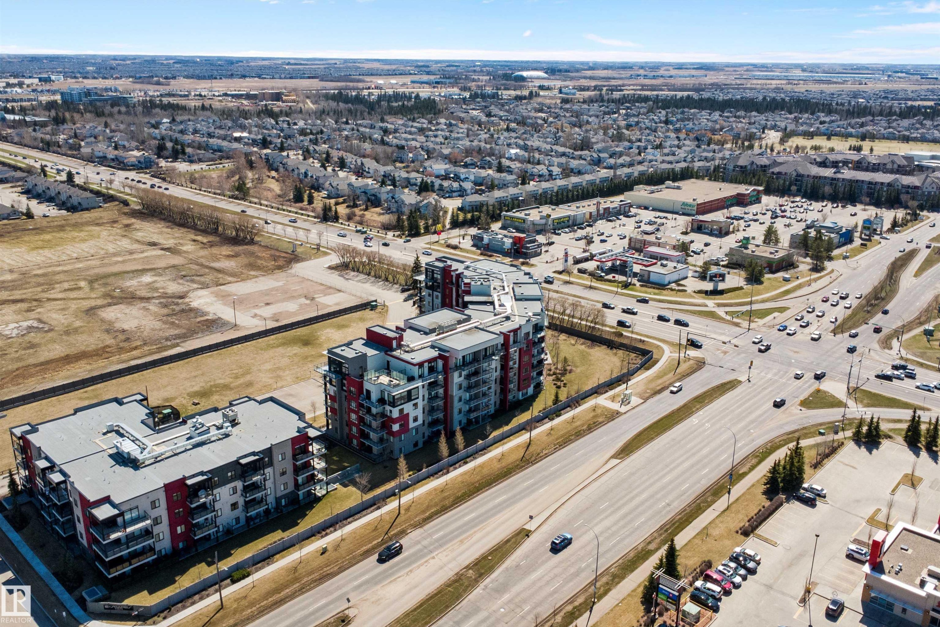 Modern multi-story residential buildings featuring contemporary architecture with vibrant red and gray facade panels. - 307 11080 Ellerslie Rd Sw, Edmonton, AB