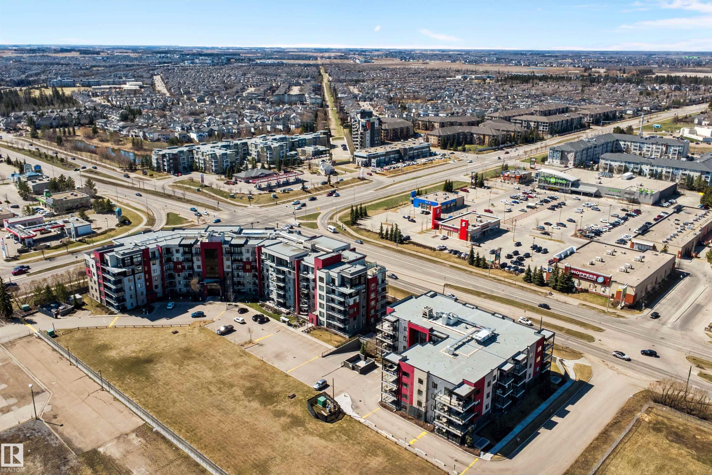 Modern multi-story residential buildings featuring contemporary architecture with vibrant red and gray facade panels. - 307 11080 Ellerslie Rd Sw, Edmonton, AB