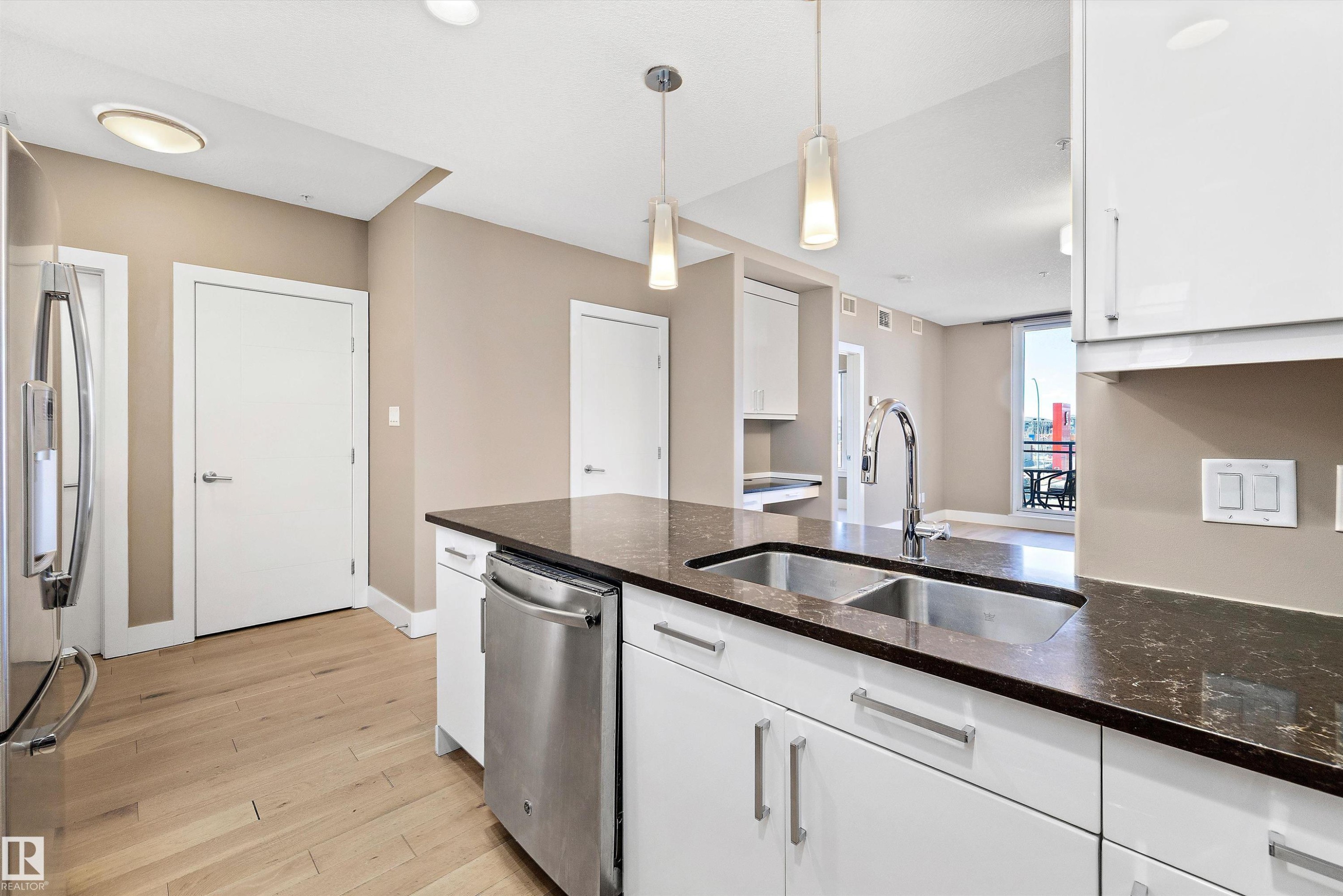 Modern kitchen featuring white cabinetry with silver hardware, dark quartz countertops, and a stainless steel double sink with a gooseneck faucet. - 307 11080 Ellerslie Rd Sw, Edmonton, AB