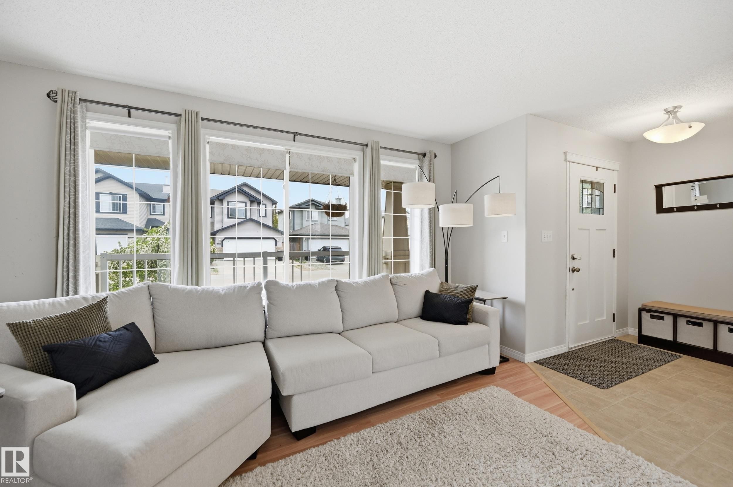 Living area featuring multiple large windows, wood-finish flooring, a front entry door with decorative glass, and tile flooring at the entry - 11628 167A Avenue, Edmonton, AB - Indoor Photo Showing Living Room
