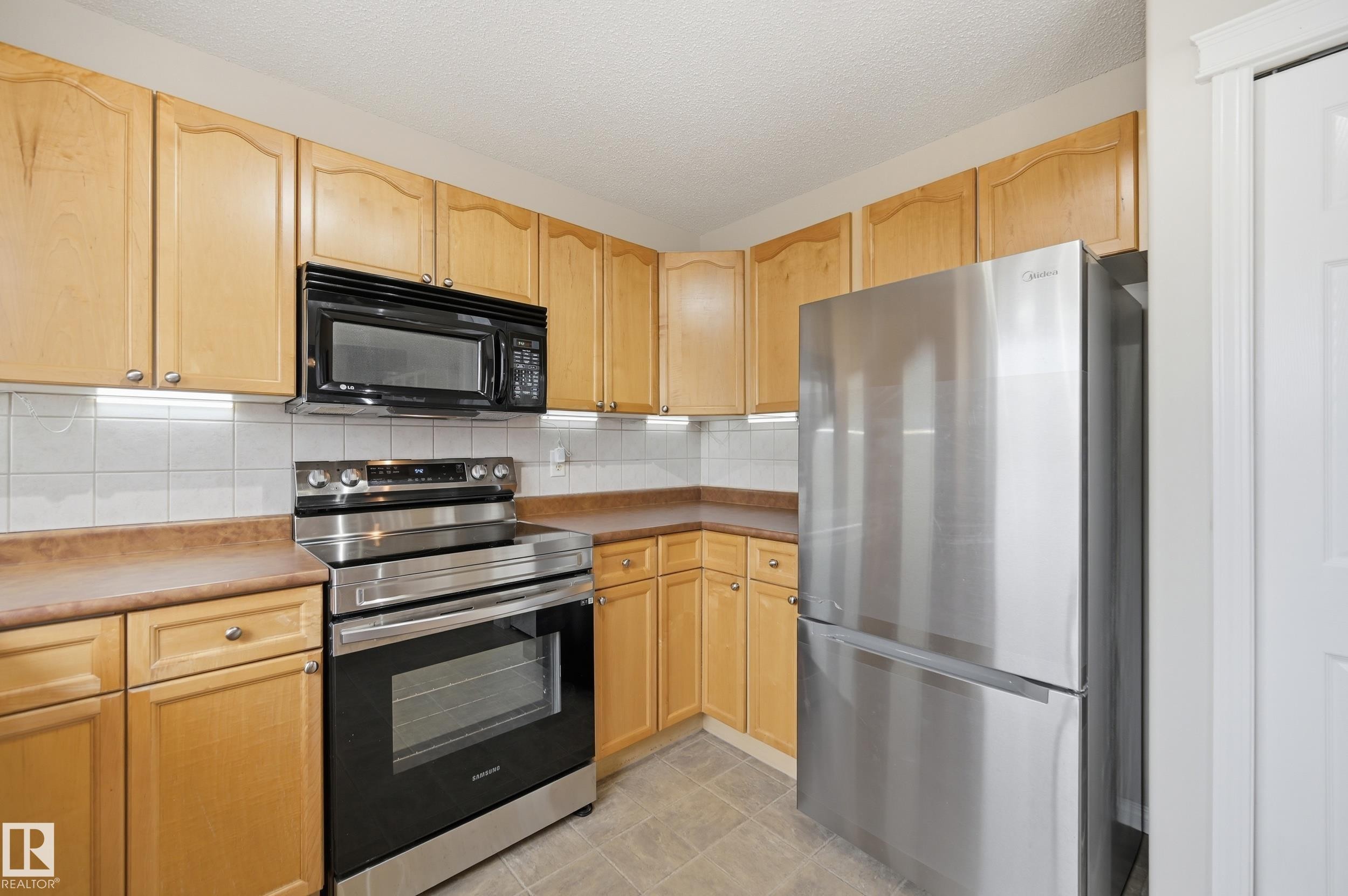 Kitchen featuring natural wood-finish cabinetry, stainless steel appliances, a white tile backsplash, and light-toned countertops - 11628 167A Avenue, Edmonton, AB - Indoor Photo Showing Kitchen With Stainless Steel Kitchen
