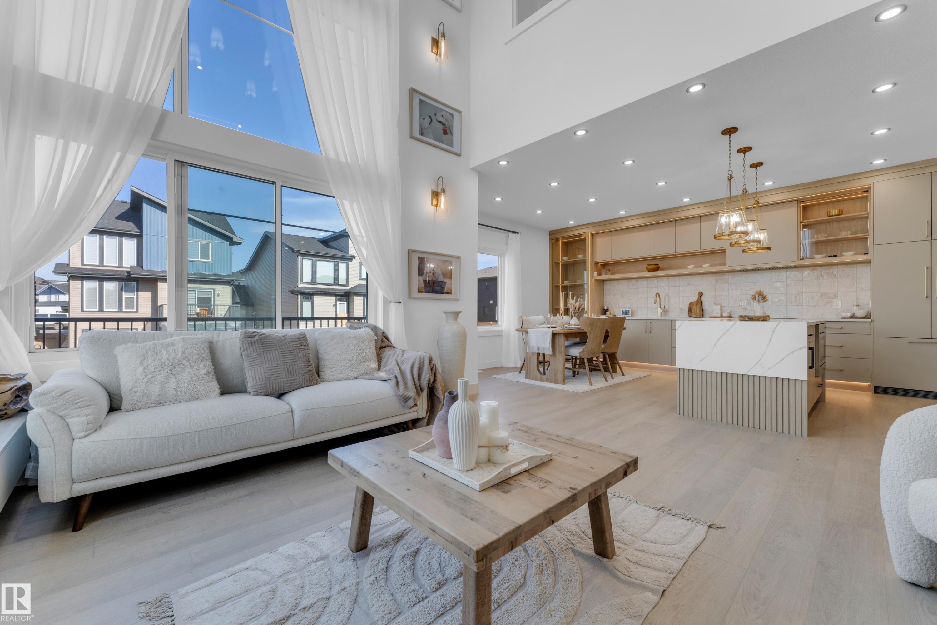 Open-concept living space featuring high ceilings, expansive window wall with sheer drapes, wood-finish flooring, and recessed lighting - 206 Linden Loop, Leduc, AB