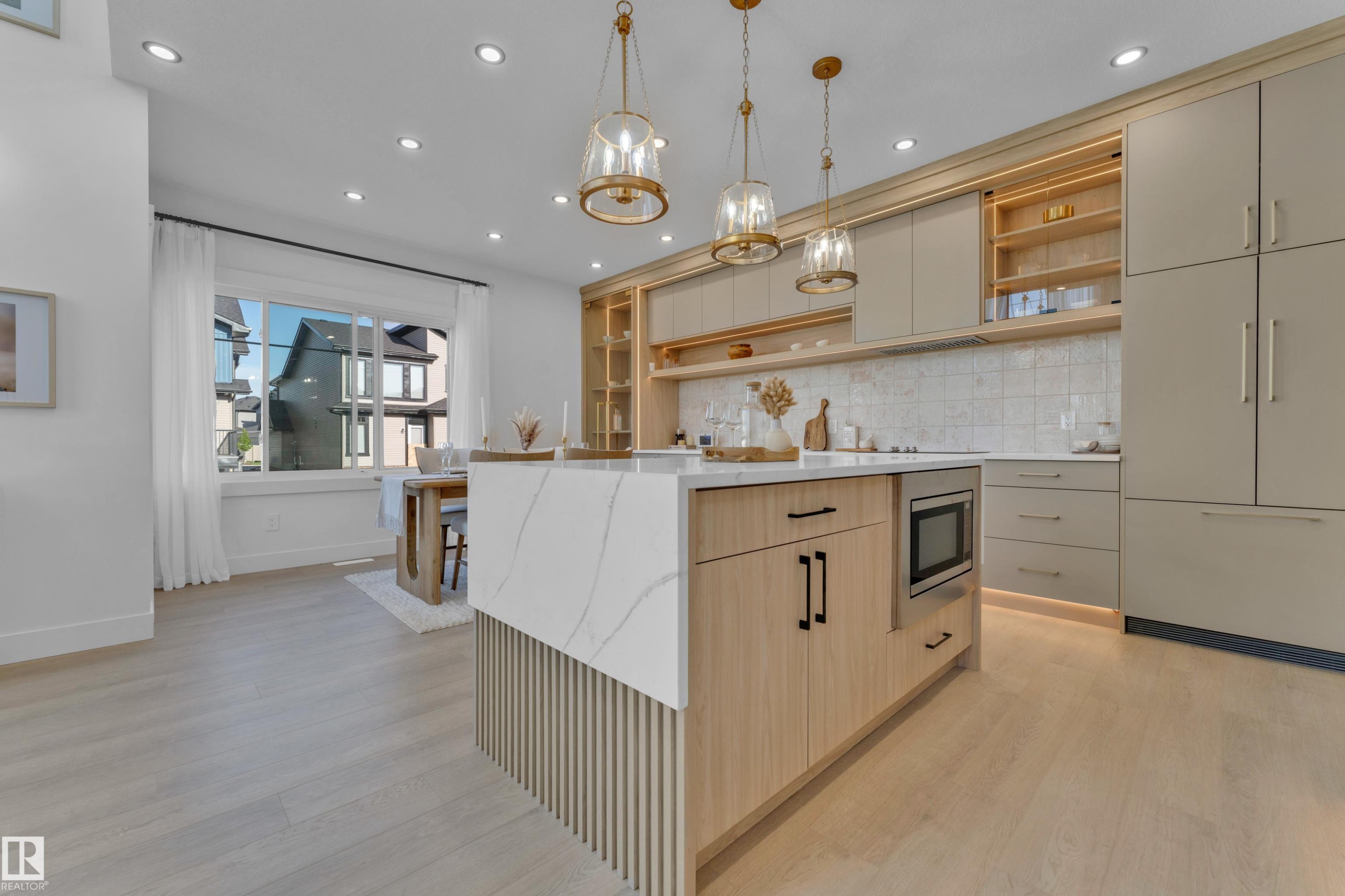 Kitchen featuring a large island with waterfall countertop, integrated microwave, and fluted paneling - 206 Linden Loop, Leduc, AB