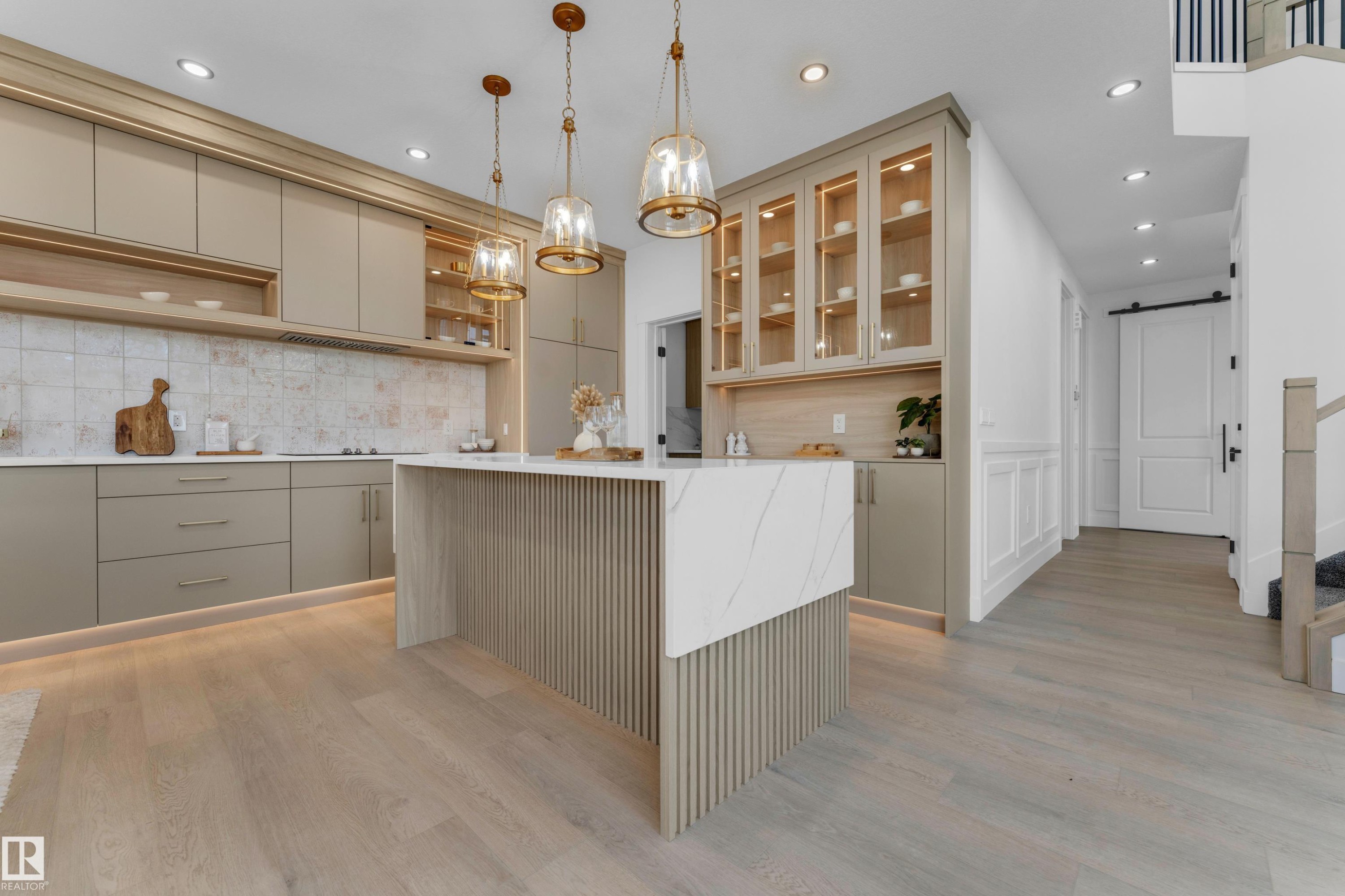 Modern kitchen featuring light-toned cabinetry, a waterfall island with slatted detailing, white countertops, and a white tile backsplash - 206 Linden Loop, Leduc, AB