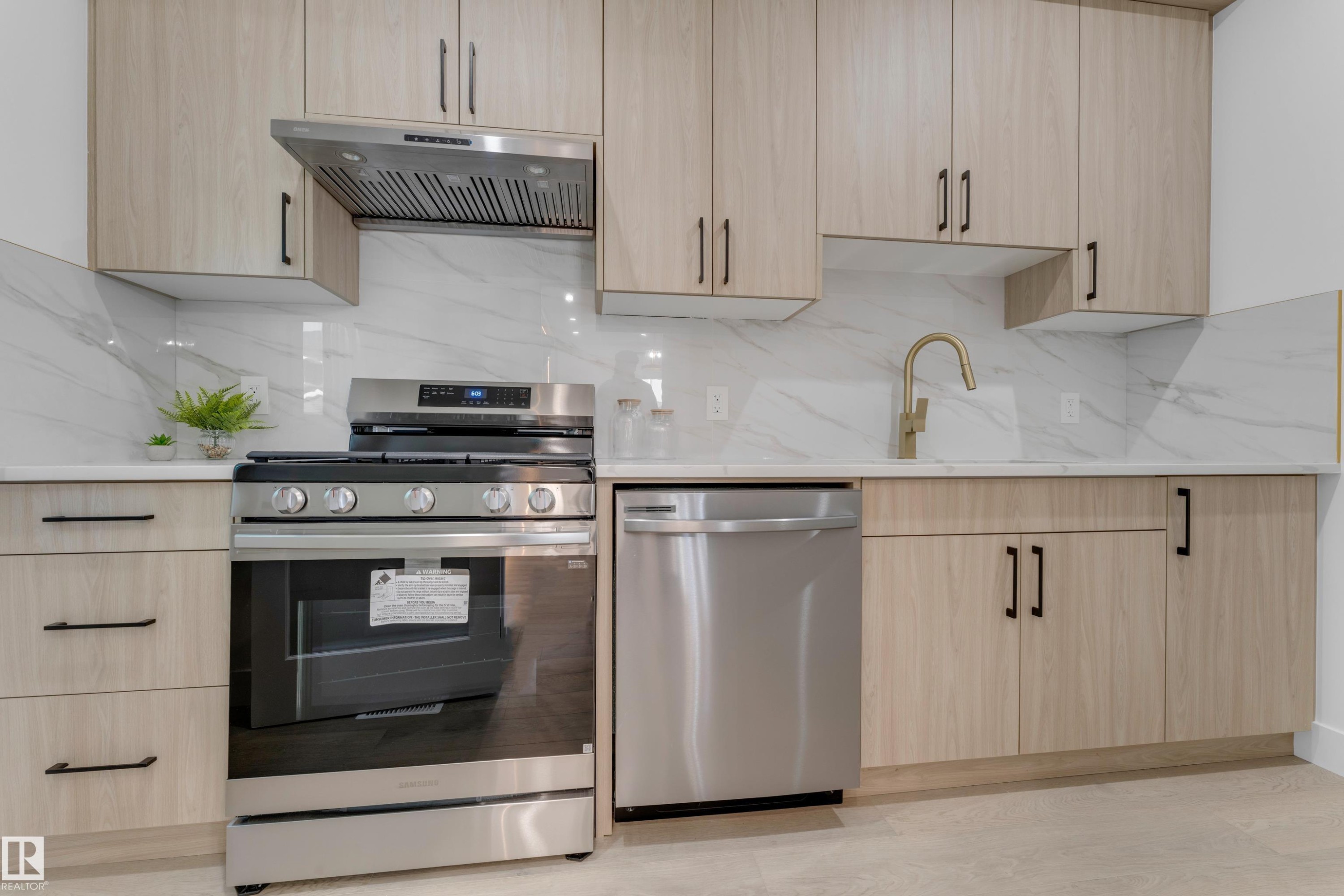 Modern kitchen featuring light wood-finish cabinetry with matte black hardware, white countertops, and a white tile backsplash - 206 Linden Loop, Leduc, AB