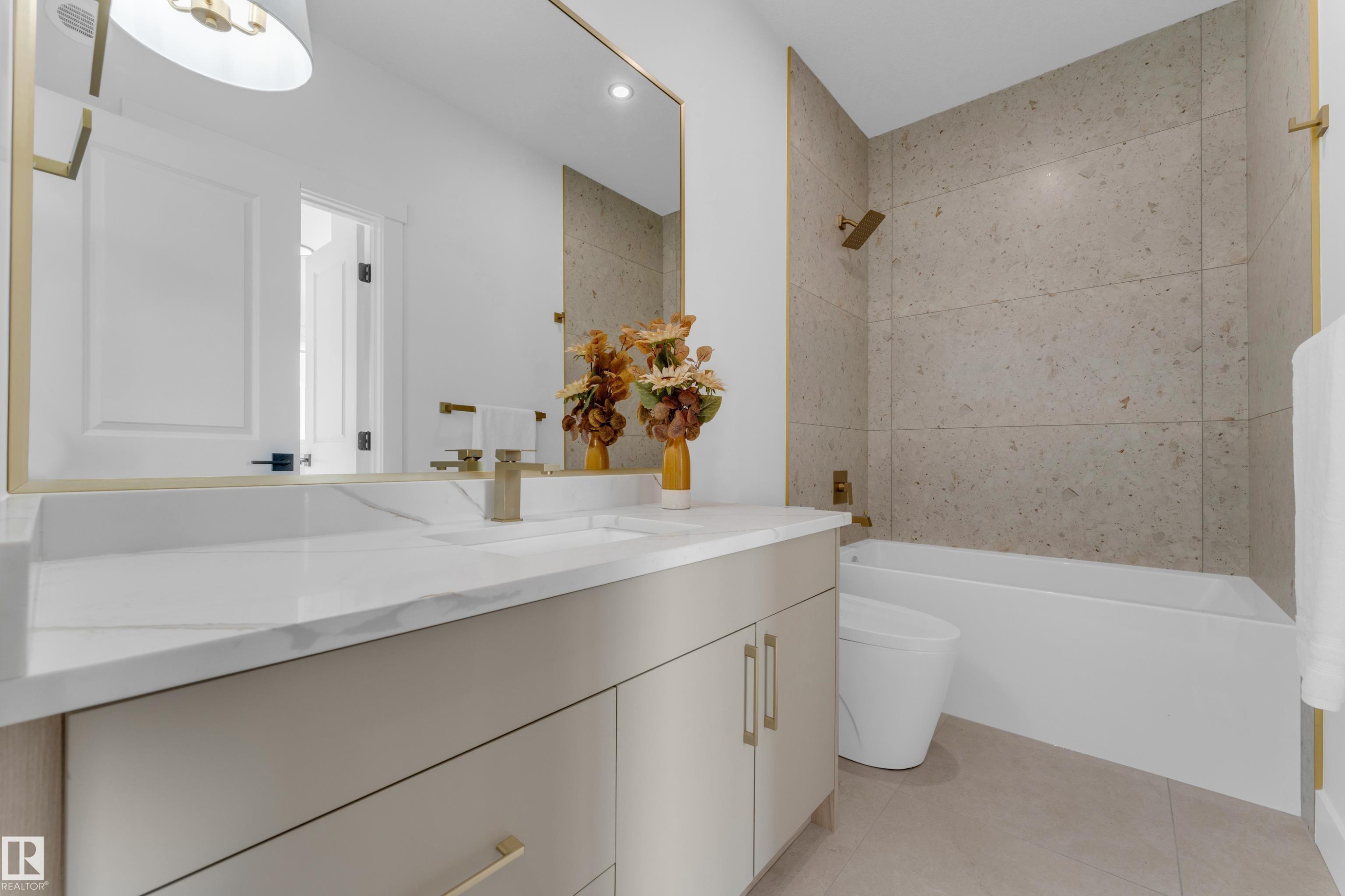 Bathroom featuring a single vanity with a white countertop and integrated sink, gold-toned fixtures, a framed mirror, a built-in bathtub, and floor-to-ceiling wall tiling in the shower area - 206 Linden Loop, Leduc, AB