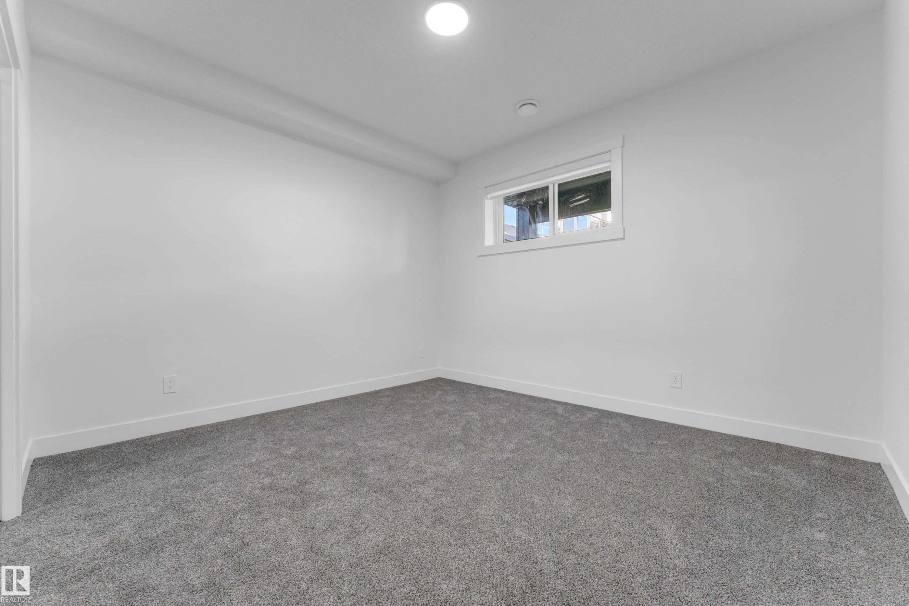 Carpeted room featuring a single window, white walls, white baseboards, and a circular ceiling light fixture - 206 Linden Loop, Leduc, AB