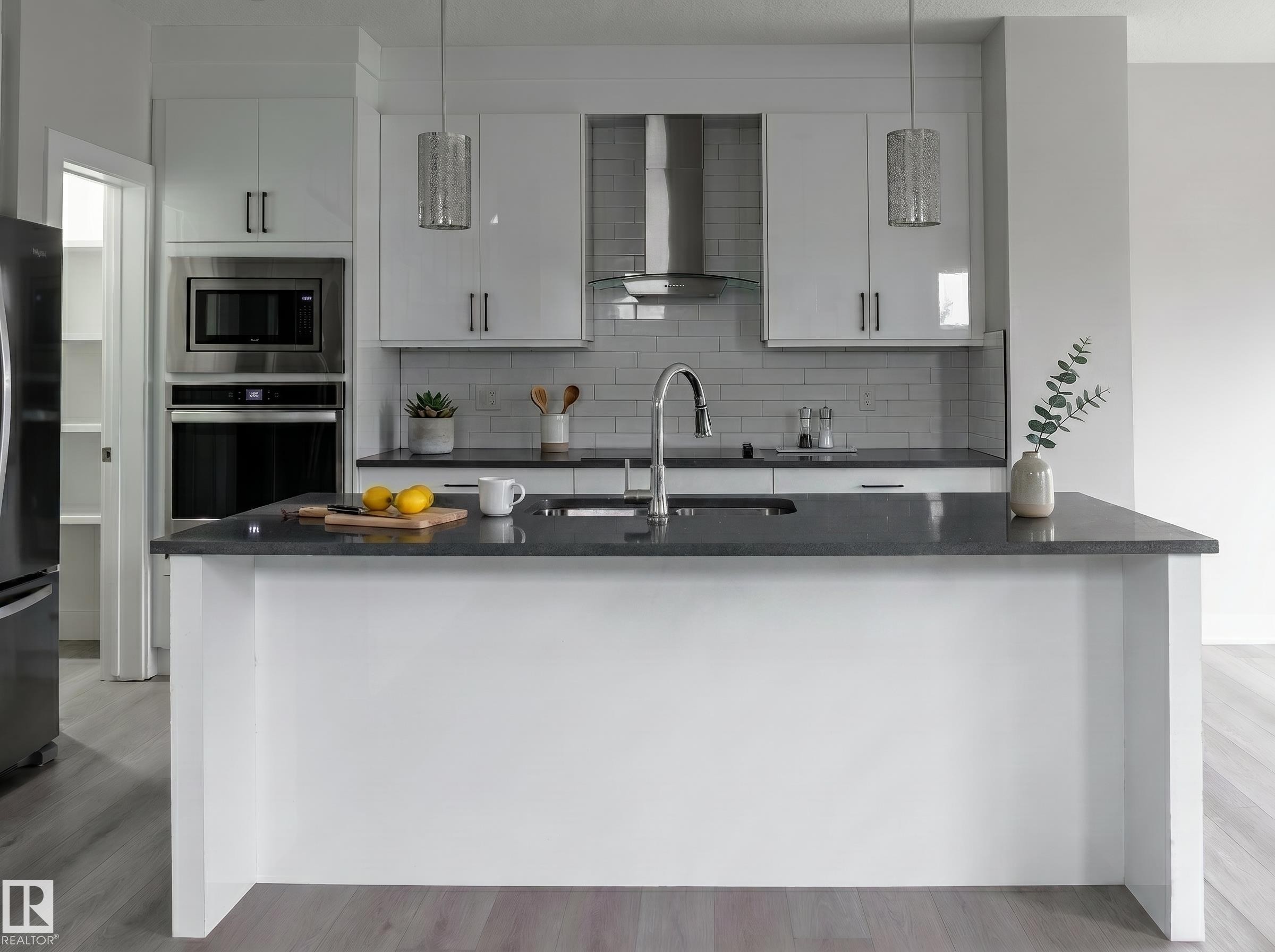 Kitchen island with dark countertop, white cabinetry, built-in stainless steel appliances, pendant lighting, and wood-finish flooring - 2104 160 Street Sw, Edmonton, AB - Indoor Photo Showing Kitchen With Upgraded Kitchen