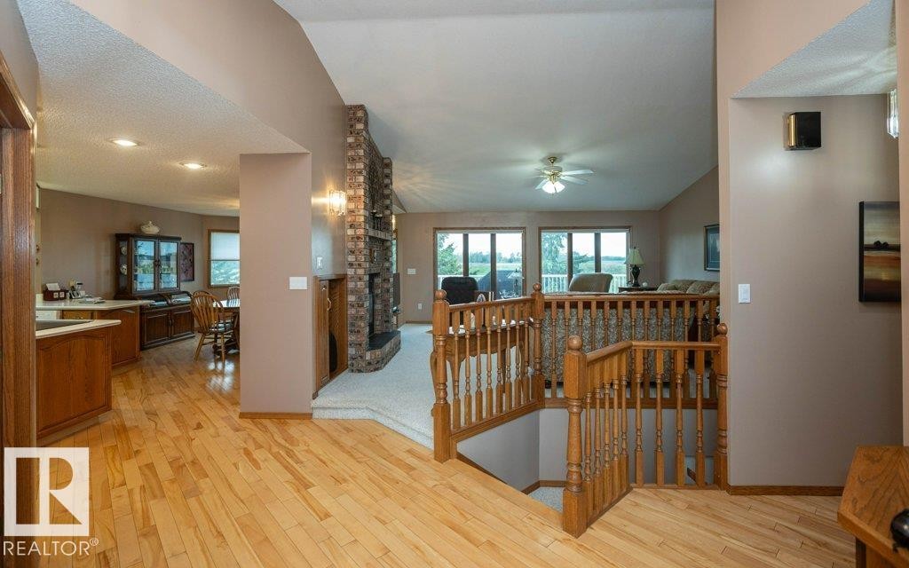 Open-concept interior featuring wood-finish flooring, a brick fireplace with a raised hearth, and natural wood railings - 60230 Rg Rd 271, Rural Westlock County, AB