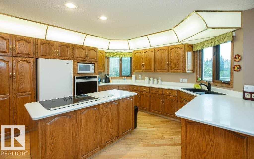 Expansive kitchen featuring wood cabinetry, light countertops, an integrated cooktop on the island, a built-in oven, and recessed lighting - 60230 Rg Rd 271, Rural Westlock County, AB