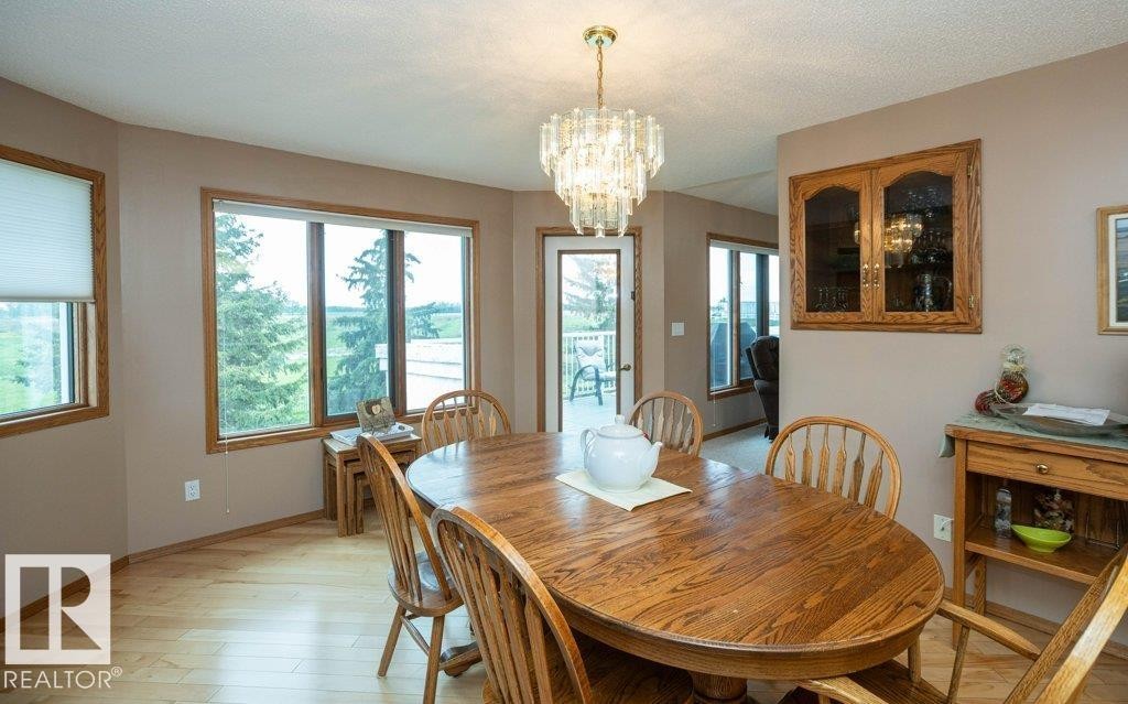 Dining area featuring wood-finish flooring, a contemporary chandelier, built-in display cabinetry, and multiple windows - 60230 Rg Rd 271, Rural Westlock County, AB
