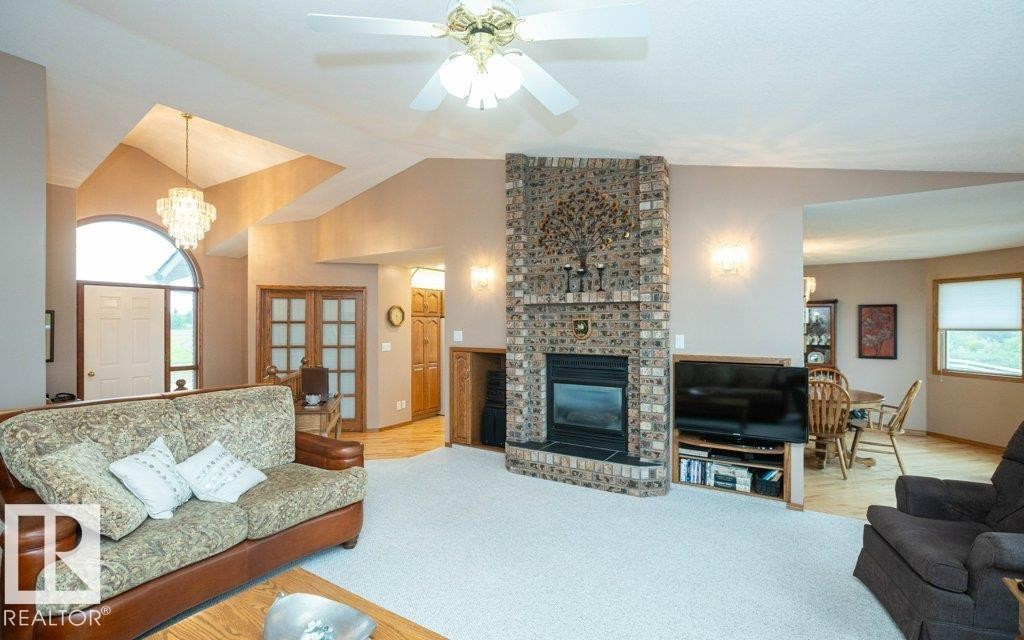 Expansive living area featuring a brick fireplace with a raised hearth, vaulted ceilings, and a crystal chandelier - 60230 Rg Rd 271, Rural Westlock County, AB