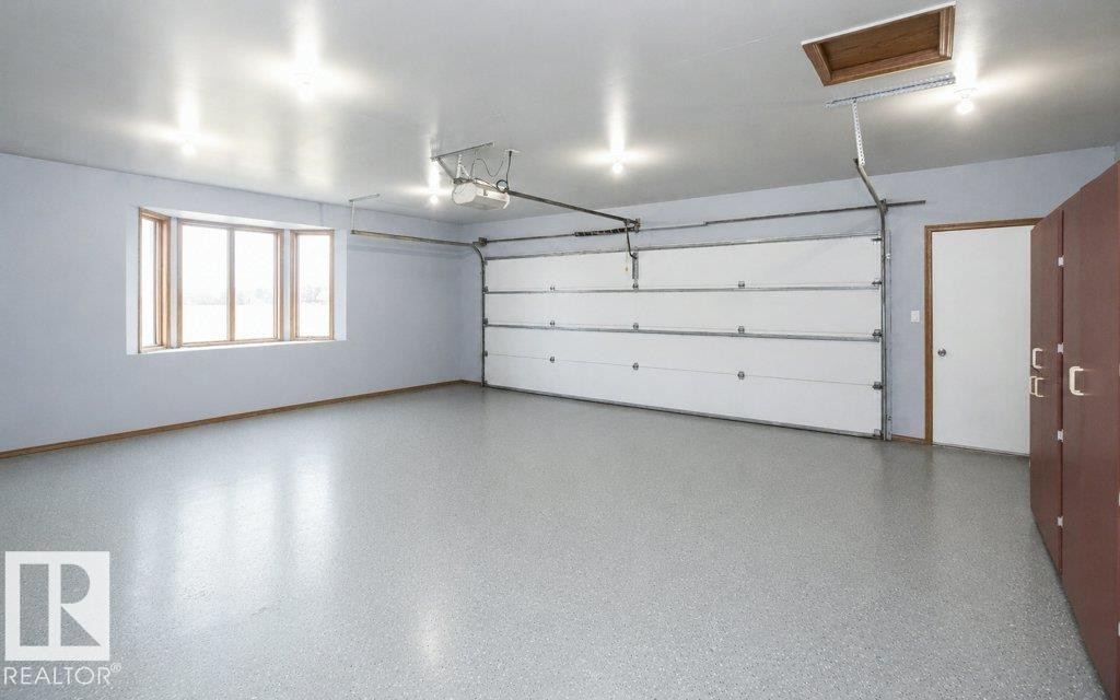 Spacious garage featuring a bay window, a sectional garage door, recessed ceiling lighting, an access door, and built-in cabinetry with metal hardware - 60230 Rg Rd 271, Rural Westlock County, AB