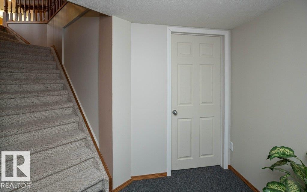 Carpeted stairway with a wooden handrail, white painted walls, and a six-panel interior door with a chrome knob - 60230 Rg Rd 271, Rural Westlock County, AB