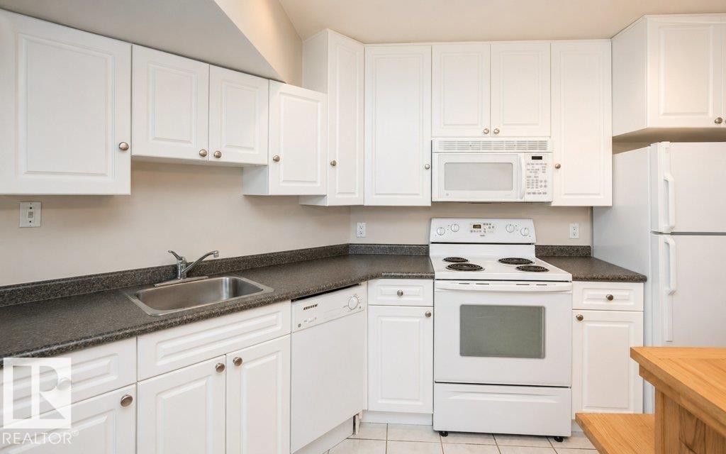 Kitchen featuring white cabinetry, dark countertops, a stainless steel sink, a range, and an over-the-range microwave - 60230 Rg Rd 271, Rural Westlock County, AB