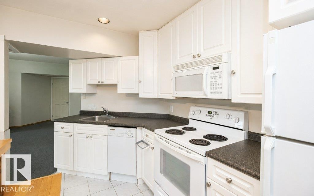 Kitchen featuring white cabinetry with silver-tone hardware, dark countertops, and white appliances - 60230 Rg Rd 271, Rural Westlock County, AB