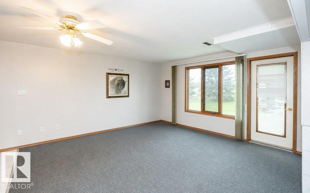 Carpeted room featuring a ceiling fan with integrated lighting, wood-trimmed windows, and a glass-paneled door - 60230 Rg Rd 271, Rural Westlock County, AB