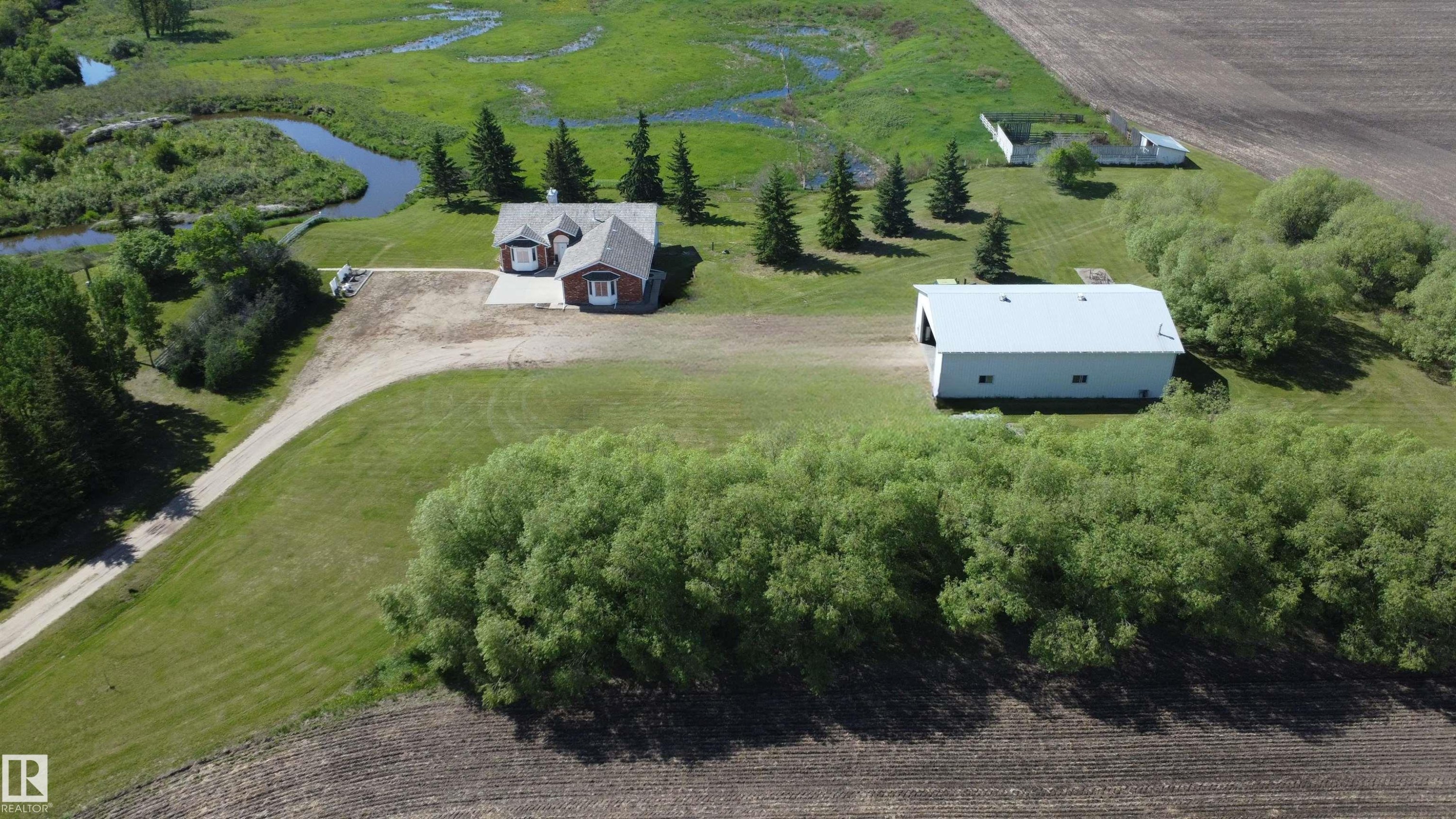 Property featuring a red brick dwelling with gray roofing, a gravel driveway, and a large metal-roofed outbuilding - 60230 Rg Rd 271, Rural Westlock County, AB