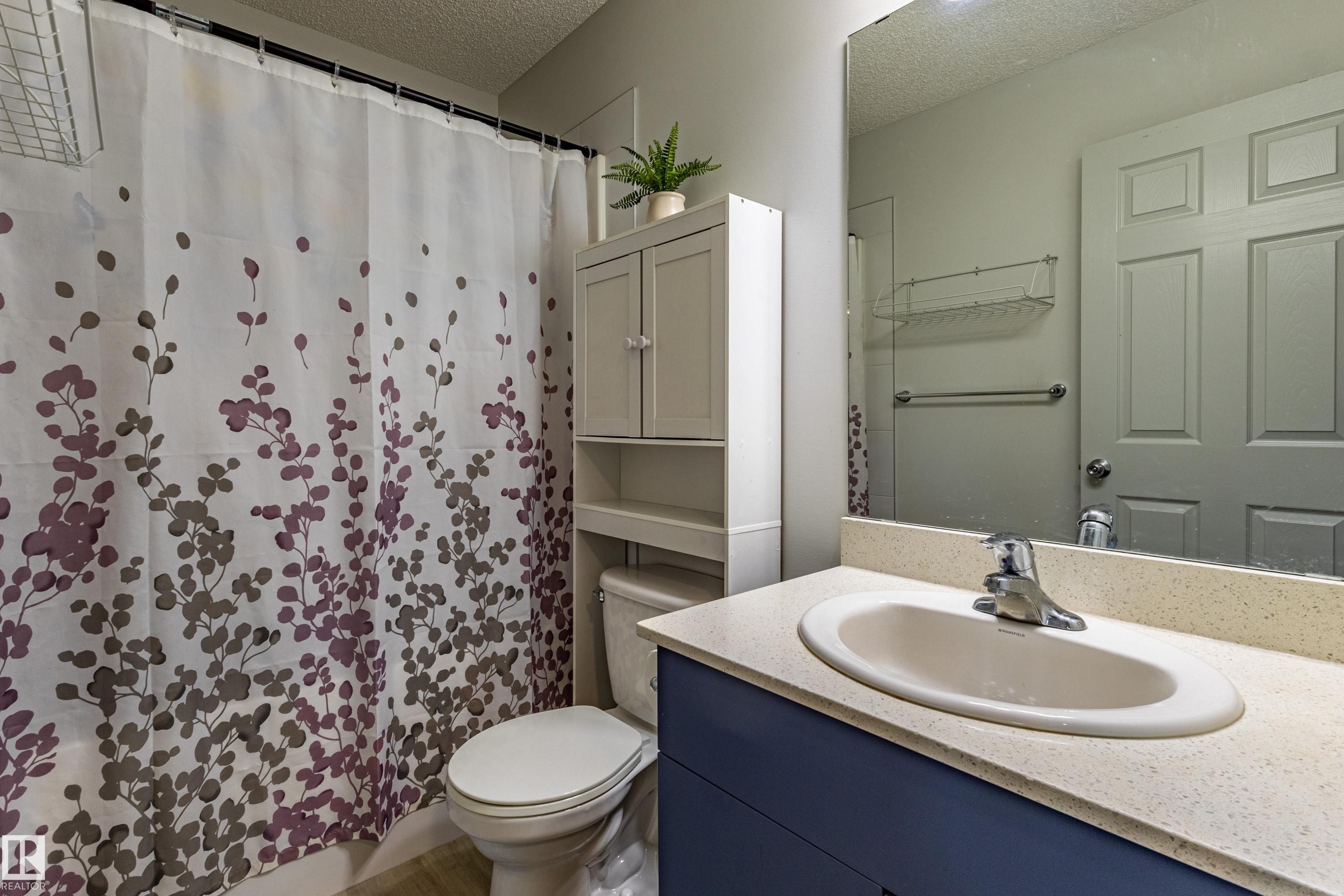Bathroom featuring a single vanity with an oval sink and chrome faucet, a light-colored countertop, and a blue base cabinet - 41 Sequoia Bend, Fort Saskatchewan, AB