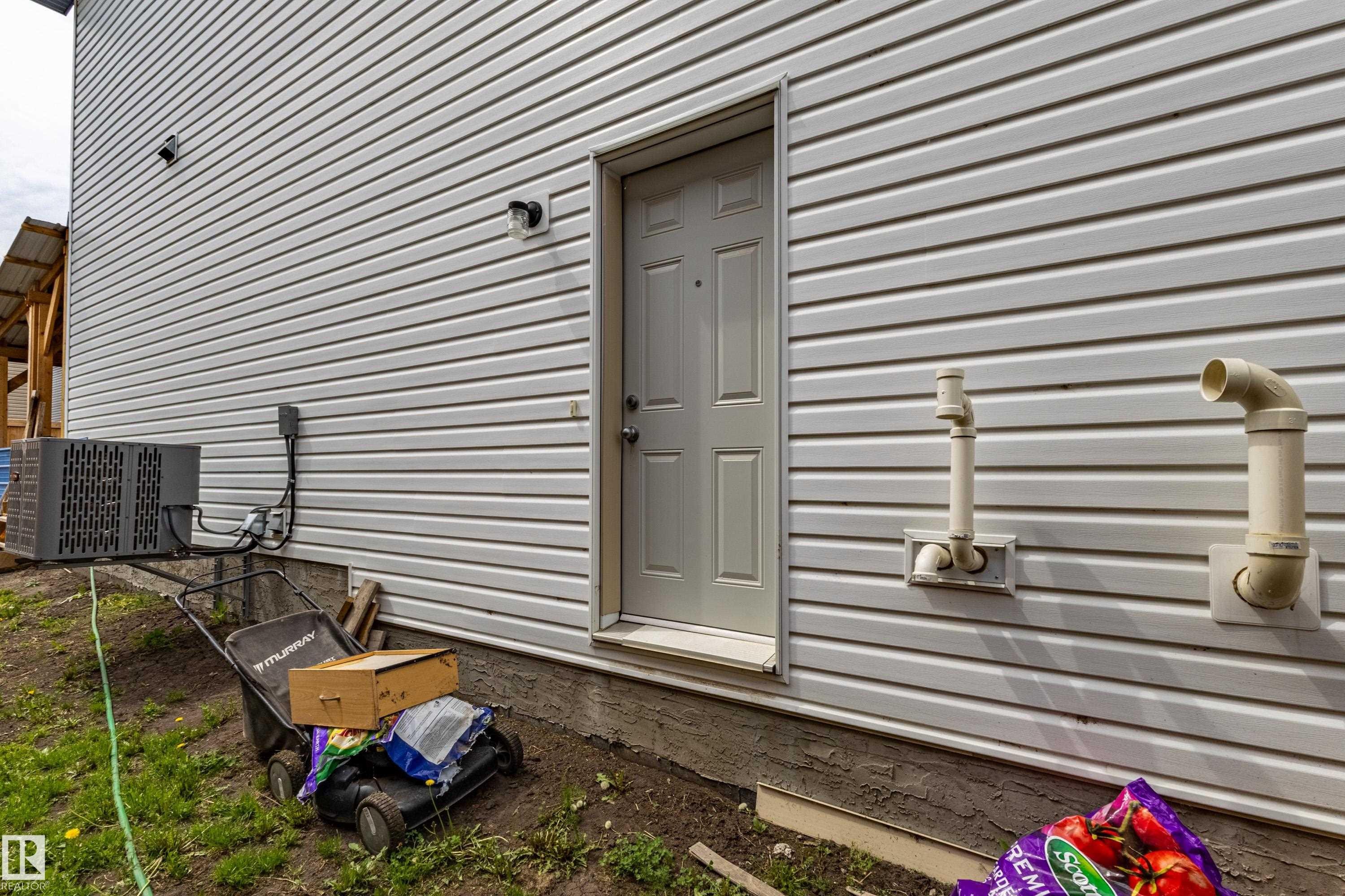White vinyl siding exterior featuring an exterior door, an HVAC unit, and foundation - 41 Sequoia Bend, Fort Saskatchewan, AB