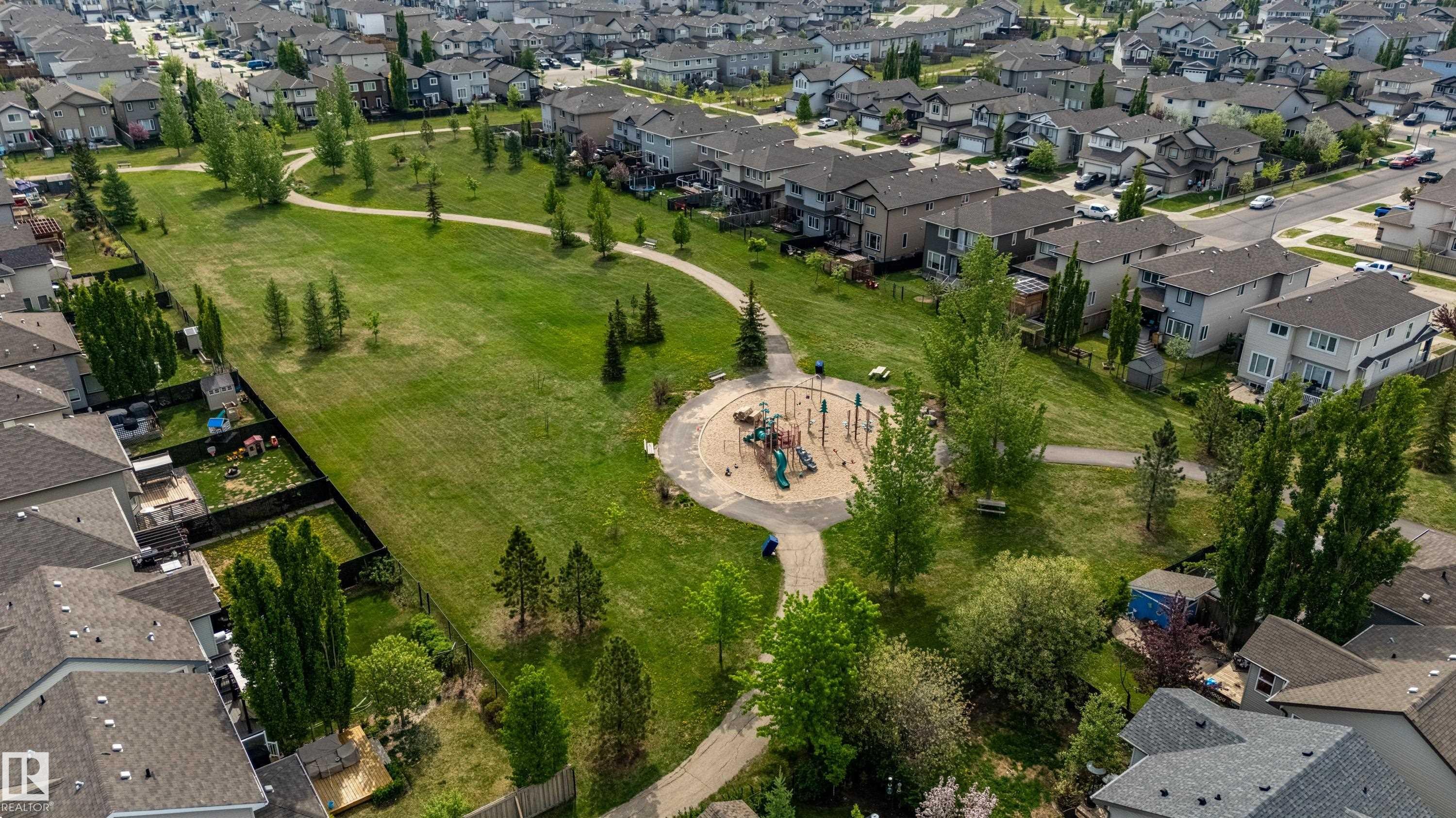Expansive green space featuring a circular playground area, paved walking paths, and numerous mature trees - 41 Sequoia Bend, Fort Saskatchewan, AB