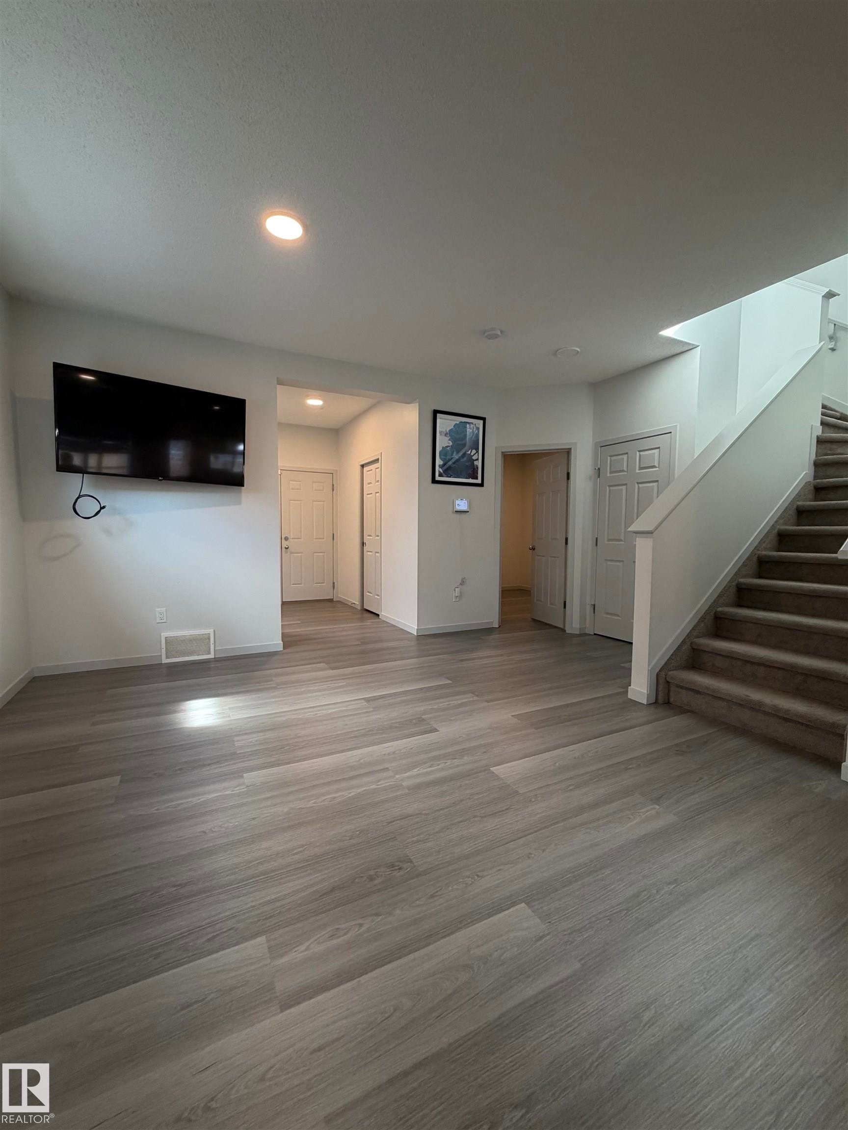 Spacious interior featuring wood-finish flooring, recessed lighting, and a carpeted staircase - 41 Sequoia Bend, Fort Saskatchewan, AB - Indoor Photo Showing Other Room