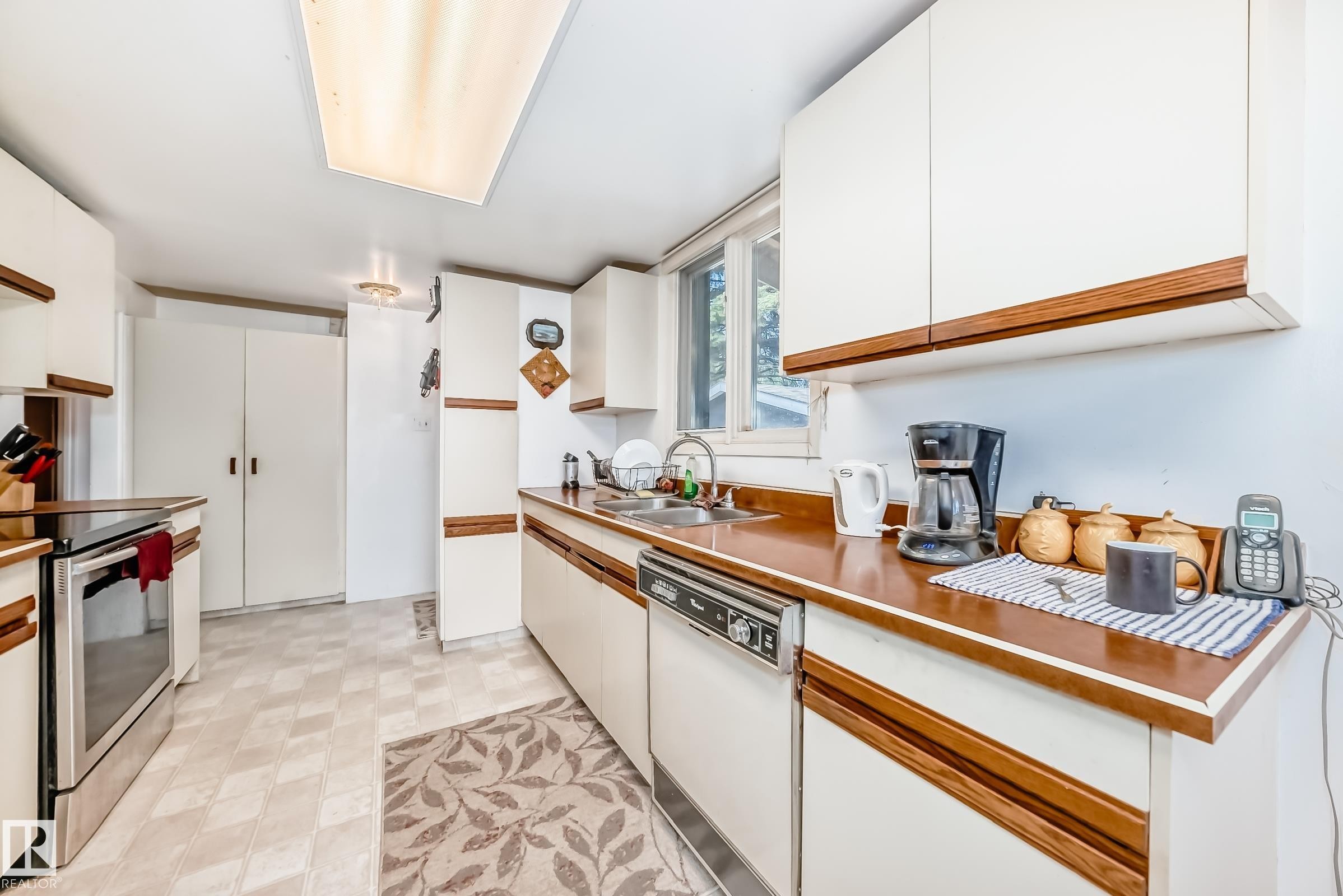 Kitchen featuring white cabinetry with wood-finish accents, wood-finish countertops, stainless steel electric range, and a built-in dishwasher - 6804 102A Avenue, Edmonton, AB
