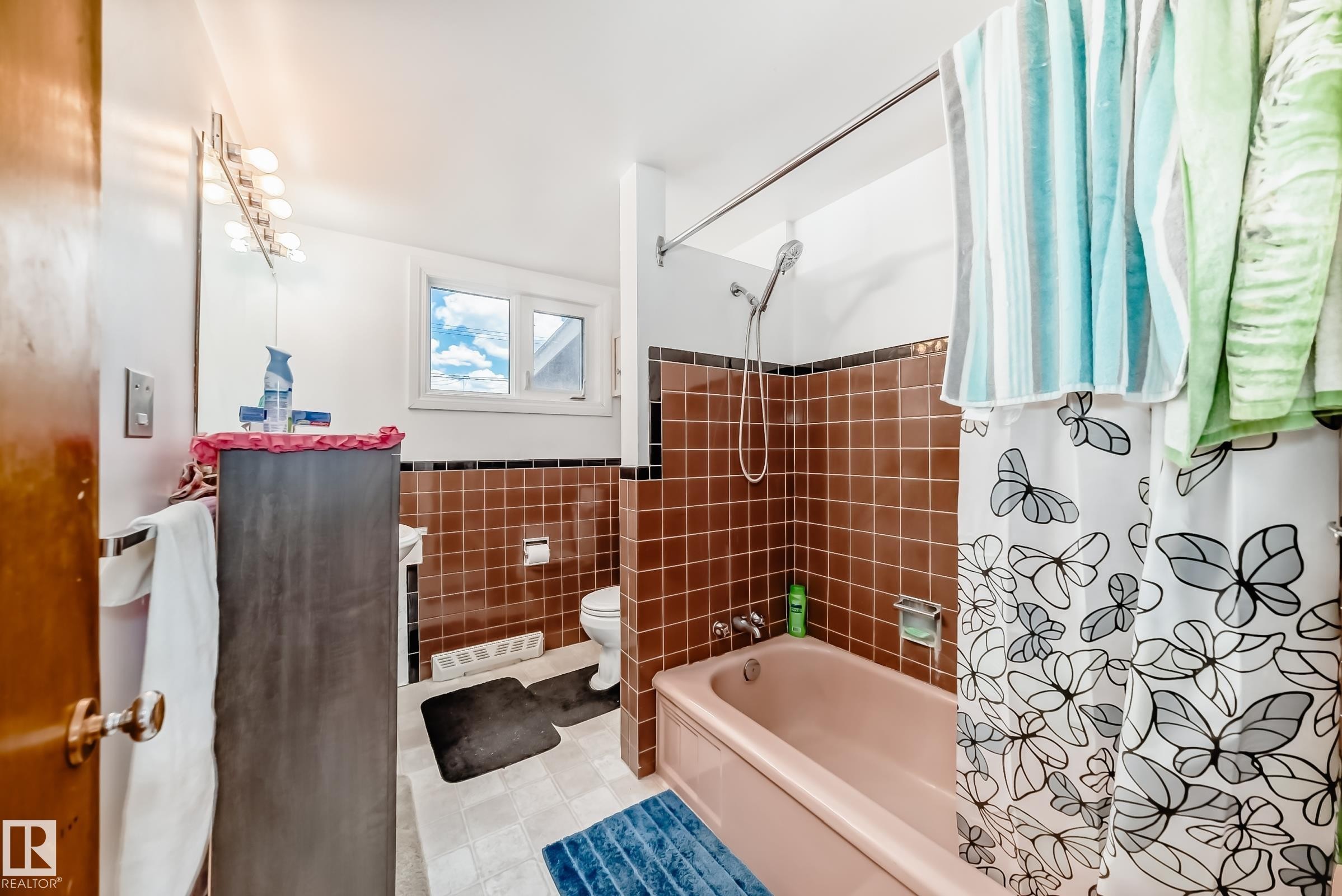 Bathroom featuring a built-in tub with shower, brown tiled walls, and a window for natural light - 6804 102A Avenue, Edmonton, AB
