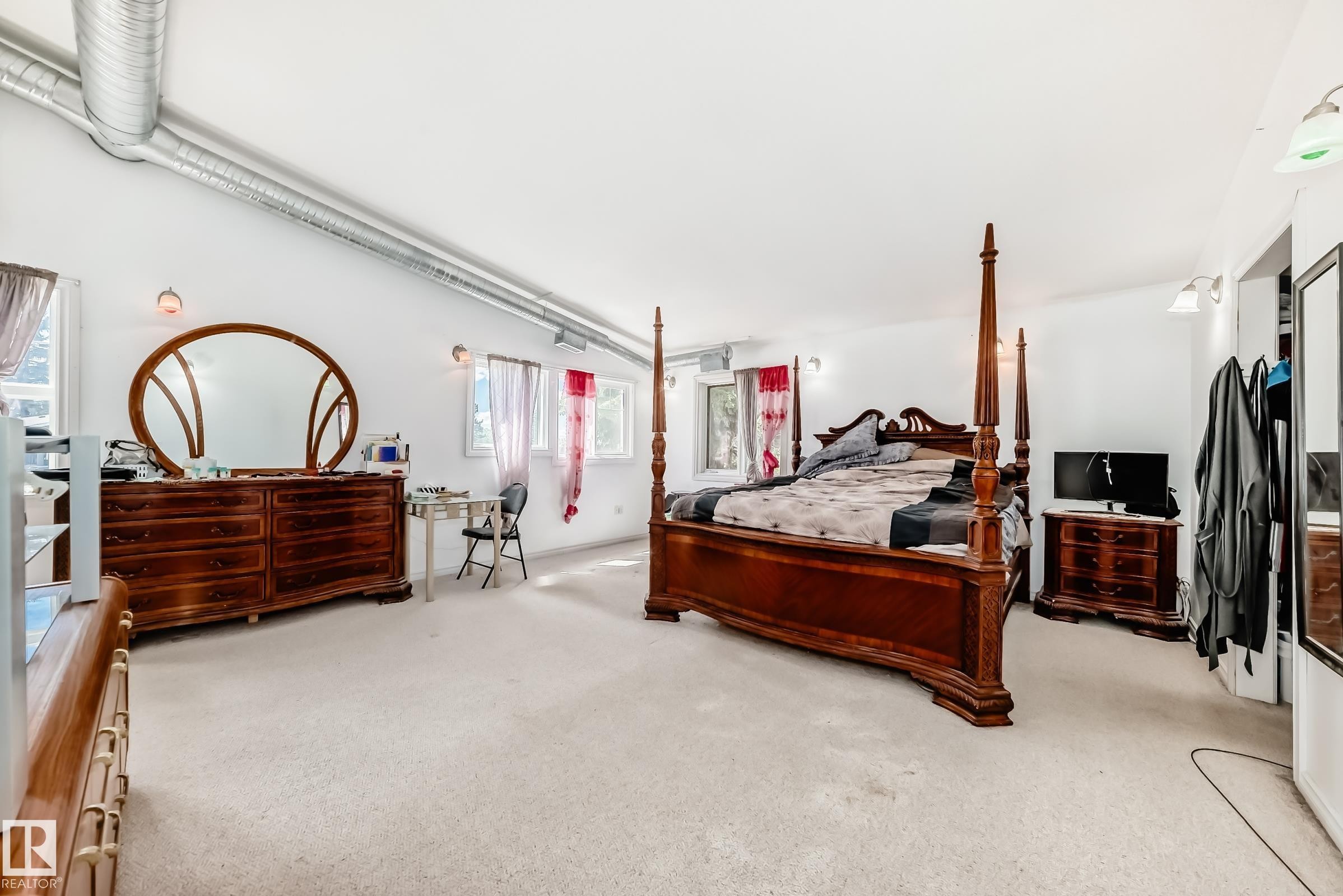 Carpeted bedroom featuring multiple windows, exposed metal ductwork, and wall-mounted light fixtures - 6804 102A Avenue, Edmonton, AB