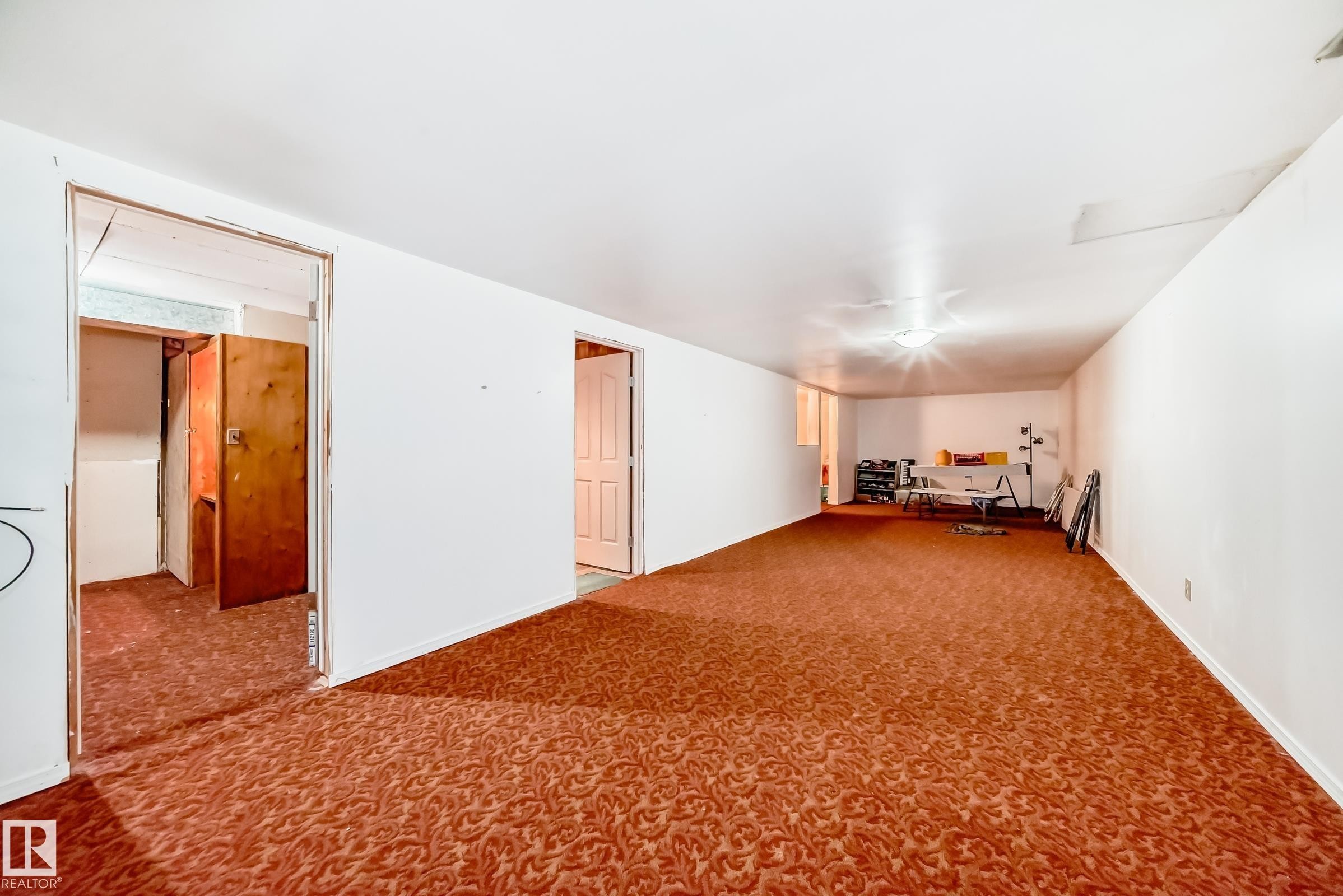 Spacious interior room featuring patterned carpeting, white painted walls, and a ceiling-mounted light fixture - 6804 102A Avenue, Edmonton, AB