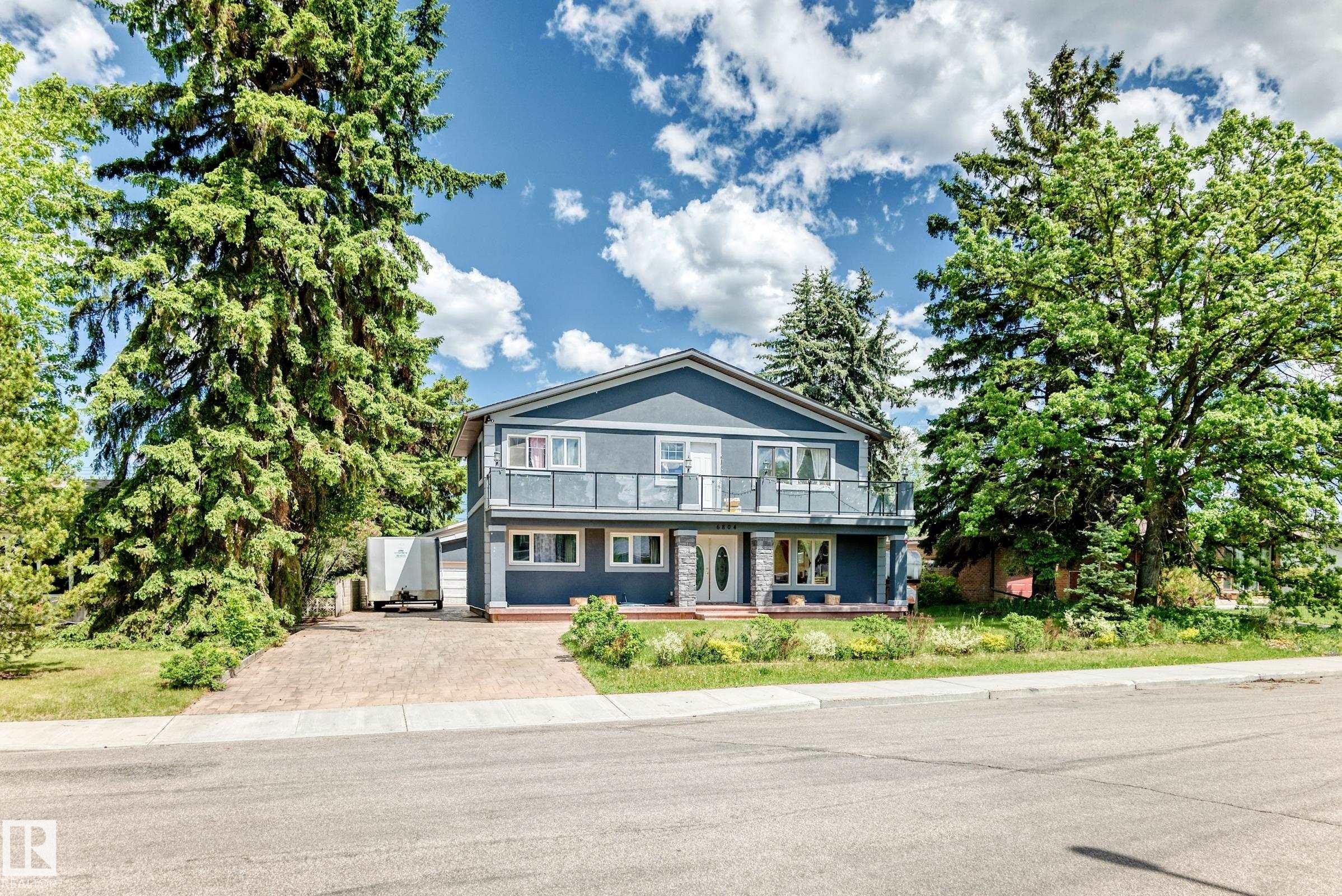 Two-story residence featuring a balcony with glass railings, stone-accented pillars, a multi-pane front door, and a paved driveway - 6804 102A Avenue, Edmonton, AB