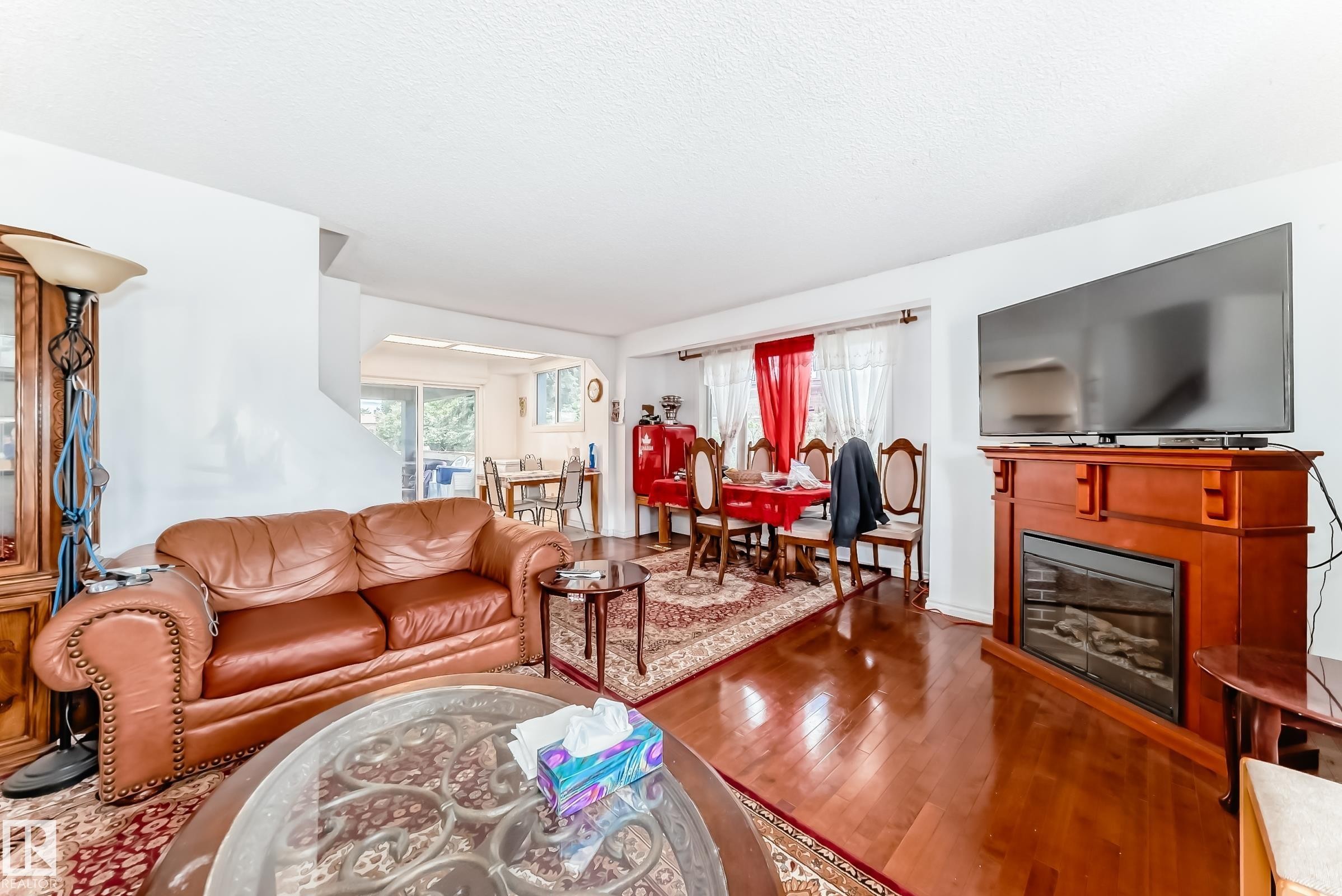 Living area featuring glossy wood-finish flooring, a built-in fireplace with a wood-tone mantel, and a recessed archway - 6804 102A Avenue, Edmonton, AB