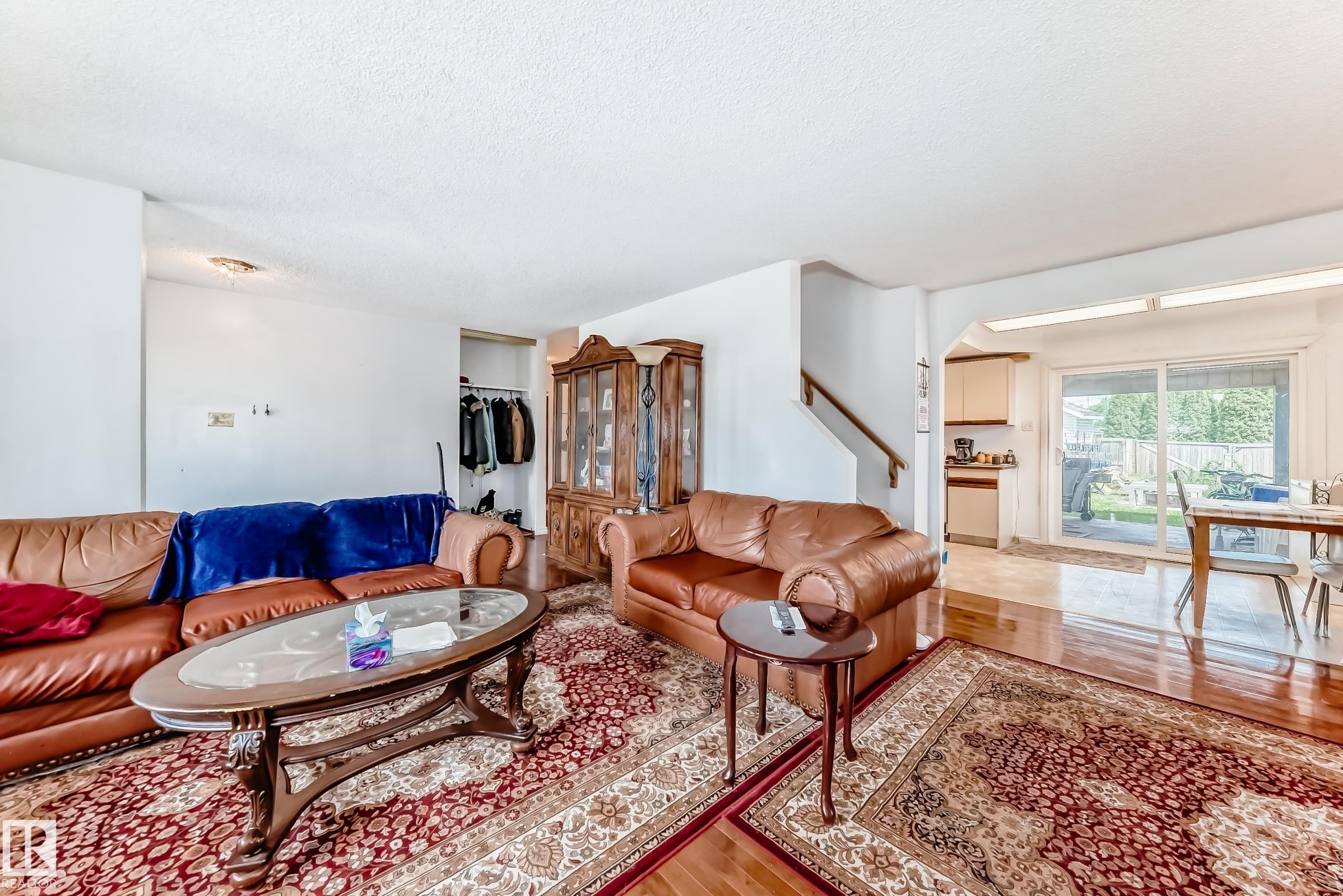 Living area featuring wood-finish flooring, a staircase with a wooden handrail, and an open doorway leading to a dining area with sliding glass doors - 6804 102A Avenue, Edmonton, AB