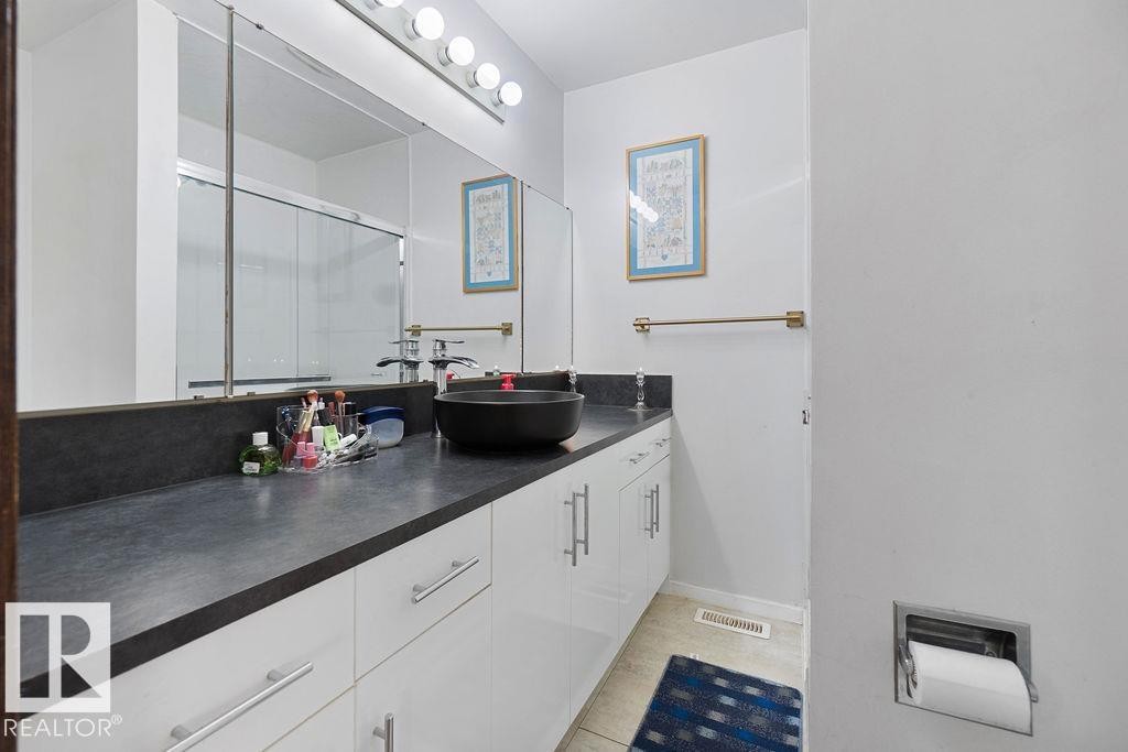 Bathroom vanity featuring a vessel sink, dark countertop, and white cabinetry with brushed nickel hardware - 712 Lee Ridge Road, Edmonton, AB