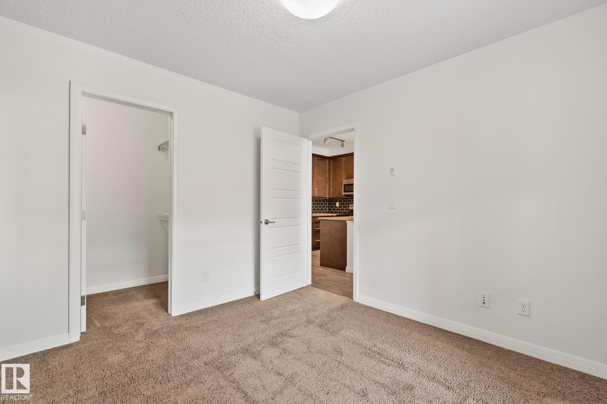 Neutral-toned carpeted room featuring a ceiling-mounted light fixture, white walls, and white trim - 217 2588 Anderson Way, Edmonton, AB