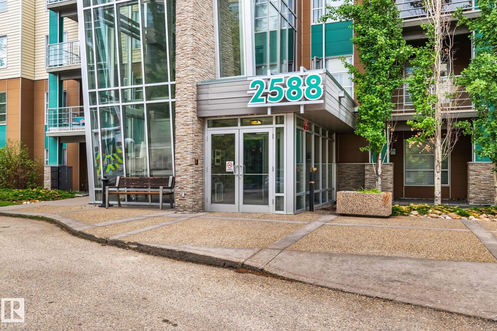 Modern building entrance featuring contemporary glass doors, a stone facade, and prominent building numbering - 217 2588 Anderson Way, Edmonton, AB