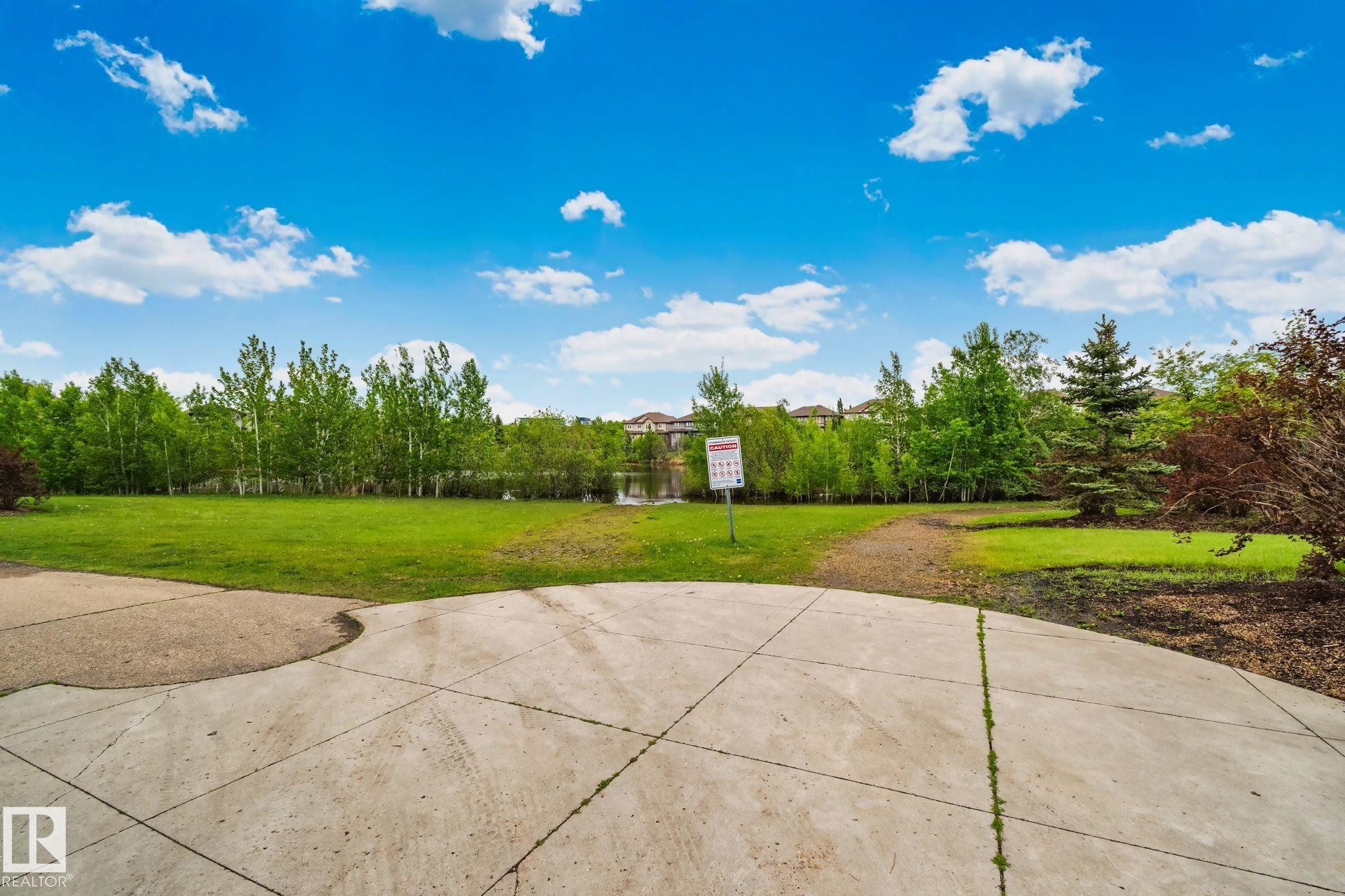 Expansive green space featuring a concrete patio, mature trees, and a distant body of water - 217 2588 Anderson Way, Edmonton, AB