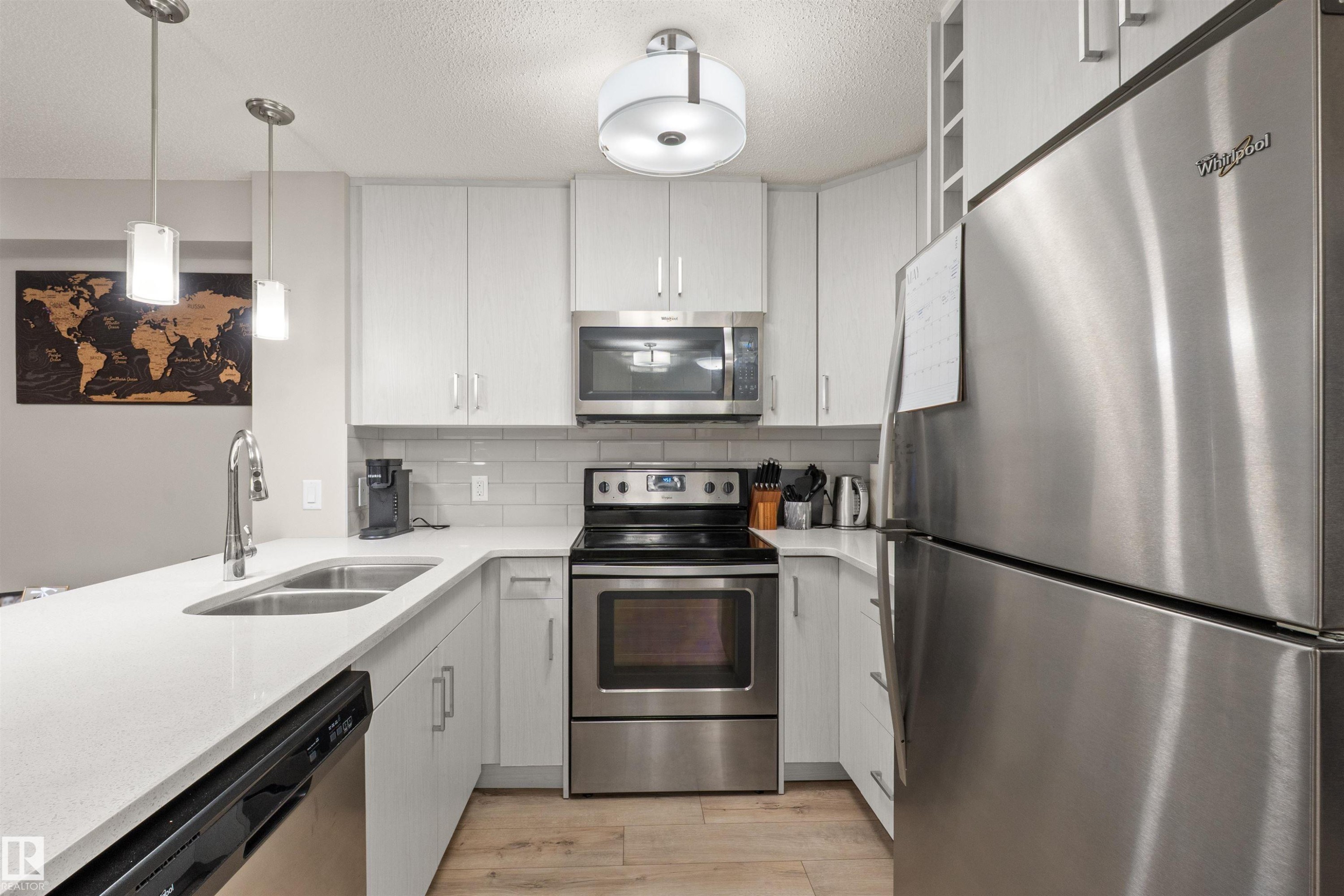 Modern kitchen featuring light-toned cabinetry, stainless steel appliances, a double basin sink, light-colored countertops, and wood-finish flooring - 210 2229 44 Avenue, Edmonton, AB