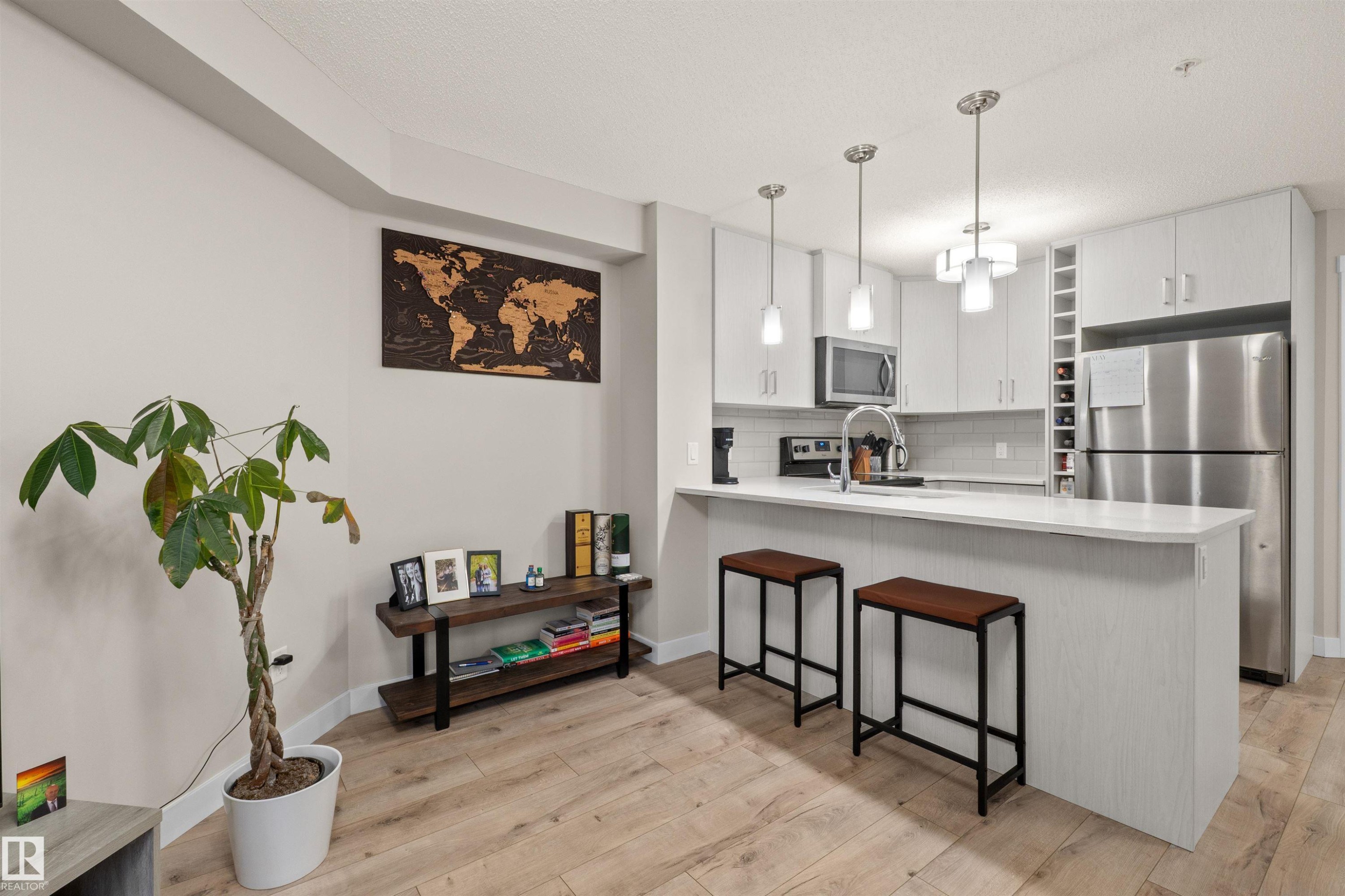 Modern kitchen featuring light-toned cabinetry, stainless steel appliances, a white subway tile backsplash, and a breakfast bar with pendant lighting - 210 2229 44 Avenue, Edmonton, AB