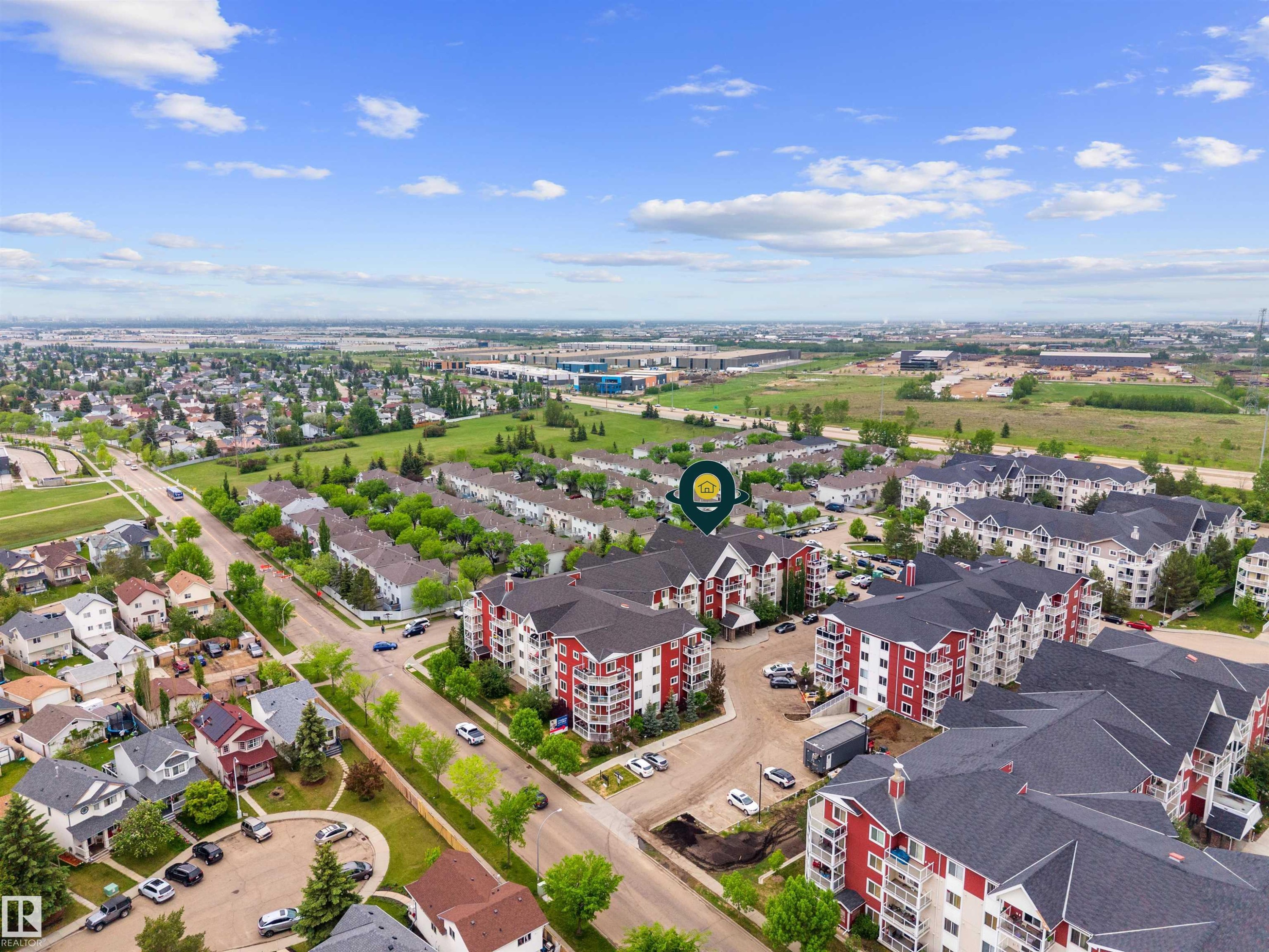 Aerial perspective showcasing a residential community with multi-story buildings featuring red and white facades and dark roofing - 210 2229 44 Avenue, Edmonton, AB