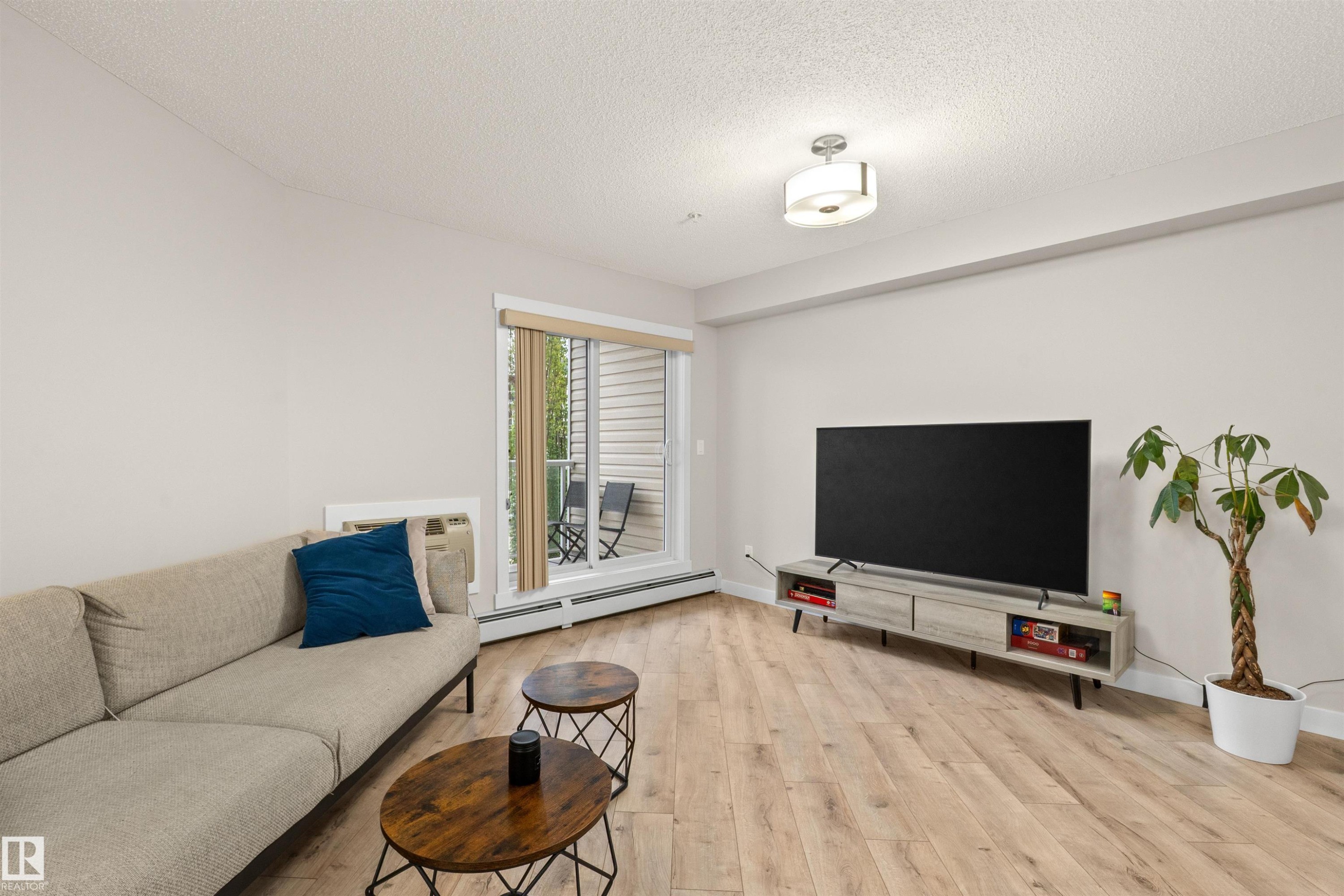 Living area featuring wood-finish flooring, a neutral color palette, and a sliding glass door opening to a private balcony - 210 2229 44 Avenue, Edmonton, AB