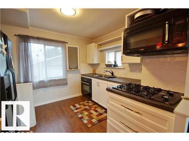 Kitchen featuring a built-in black cooktop, white cabinetry with bronze-finish hardware, dark countertops, and wood-finish flooring - 9815 160 Street, Edmonton, AB