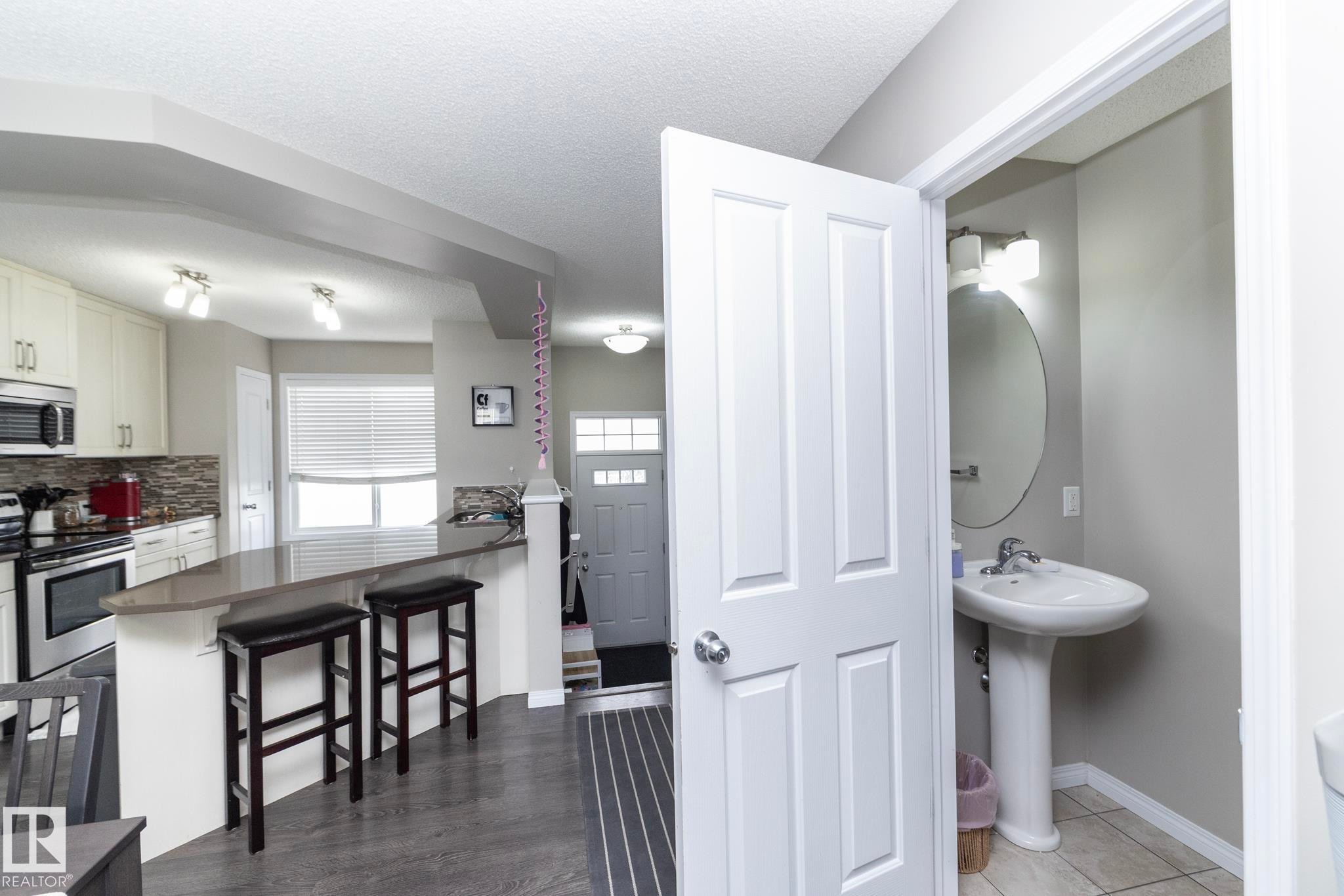 Open-concept kitchen with light cabinetry, stainless steel appliances, and a peninsula featuring a solid surface countertop and stone tile backsplash - 46 4050 Savaryn Drive, Edmonton, AB