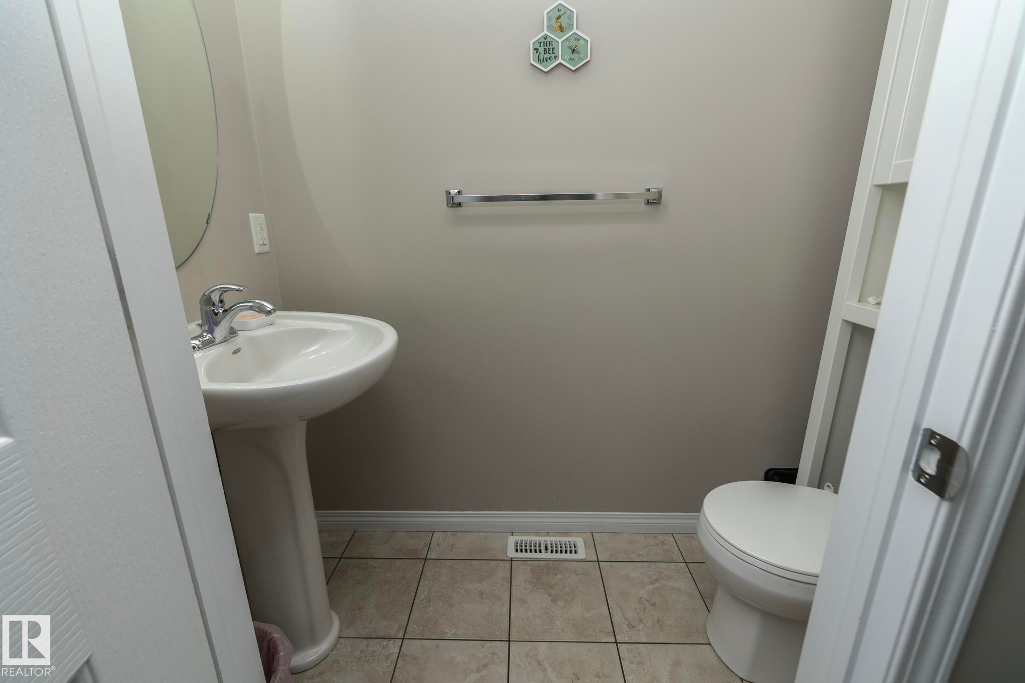 Pedestal sink with chrome faucet, complemented by a round mirror, tile flooring, and a white toilet - 46 4050 Savaryn Drive, Edmonton, AB