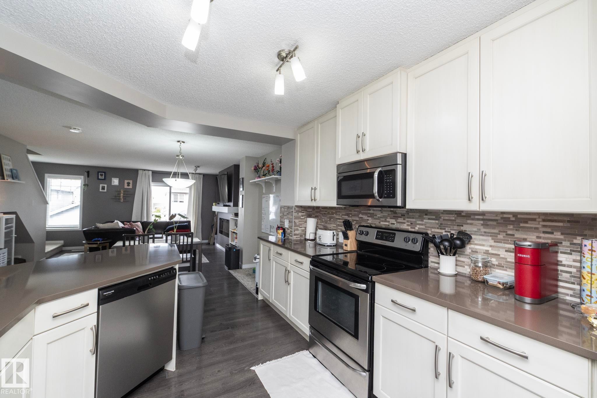 Contemporary kitchen featuring white cabinetry, stainless steel appliances, a mosaic tile backsplash, wood-finish flooring, and ample countertop space - 46 4050 Savaryn Drive, Edmonton, AB
