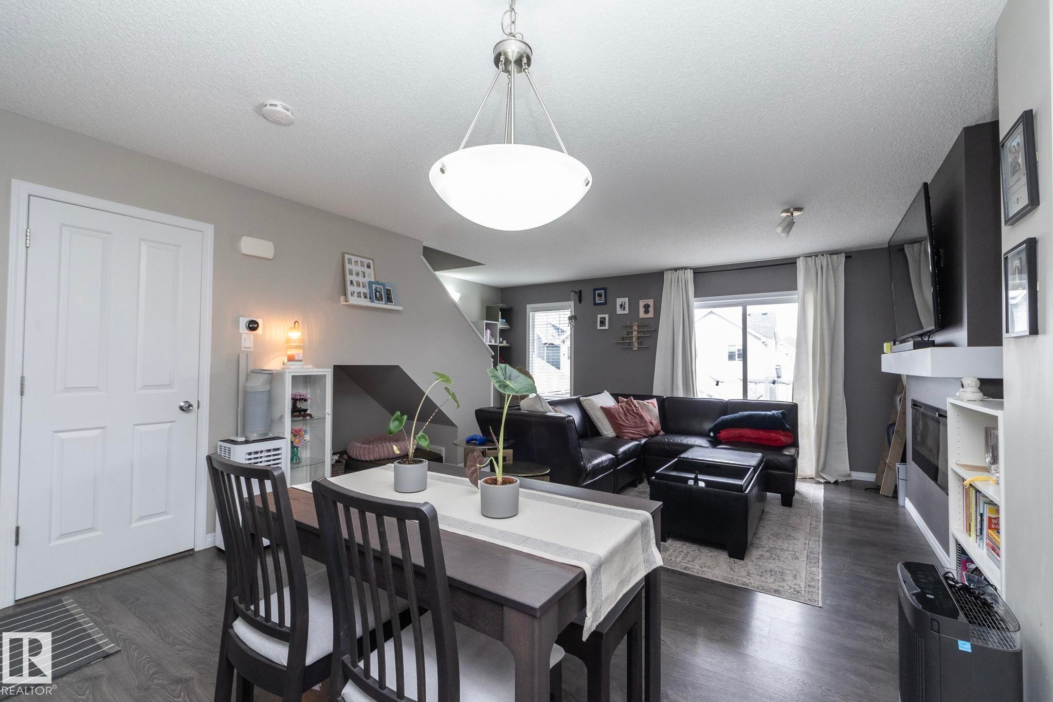 Open concept living area featuring dark wood-finish flooring, a contemporary ceiling light fixture, a built-in fireplace with a white mantel, and a sliding glass door - 46 4050 Savaryn Drive, Edmonton, AB